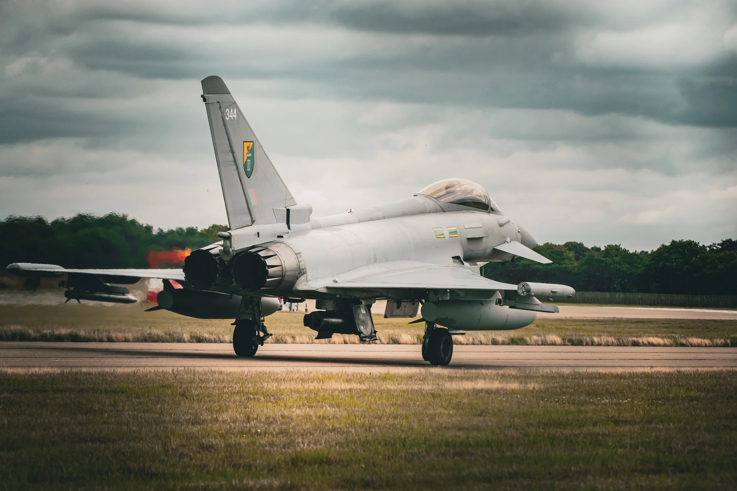 Military fighter jet on an airport runway with dark cloudy sky overhead.