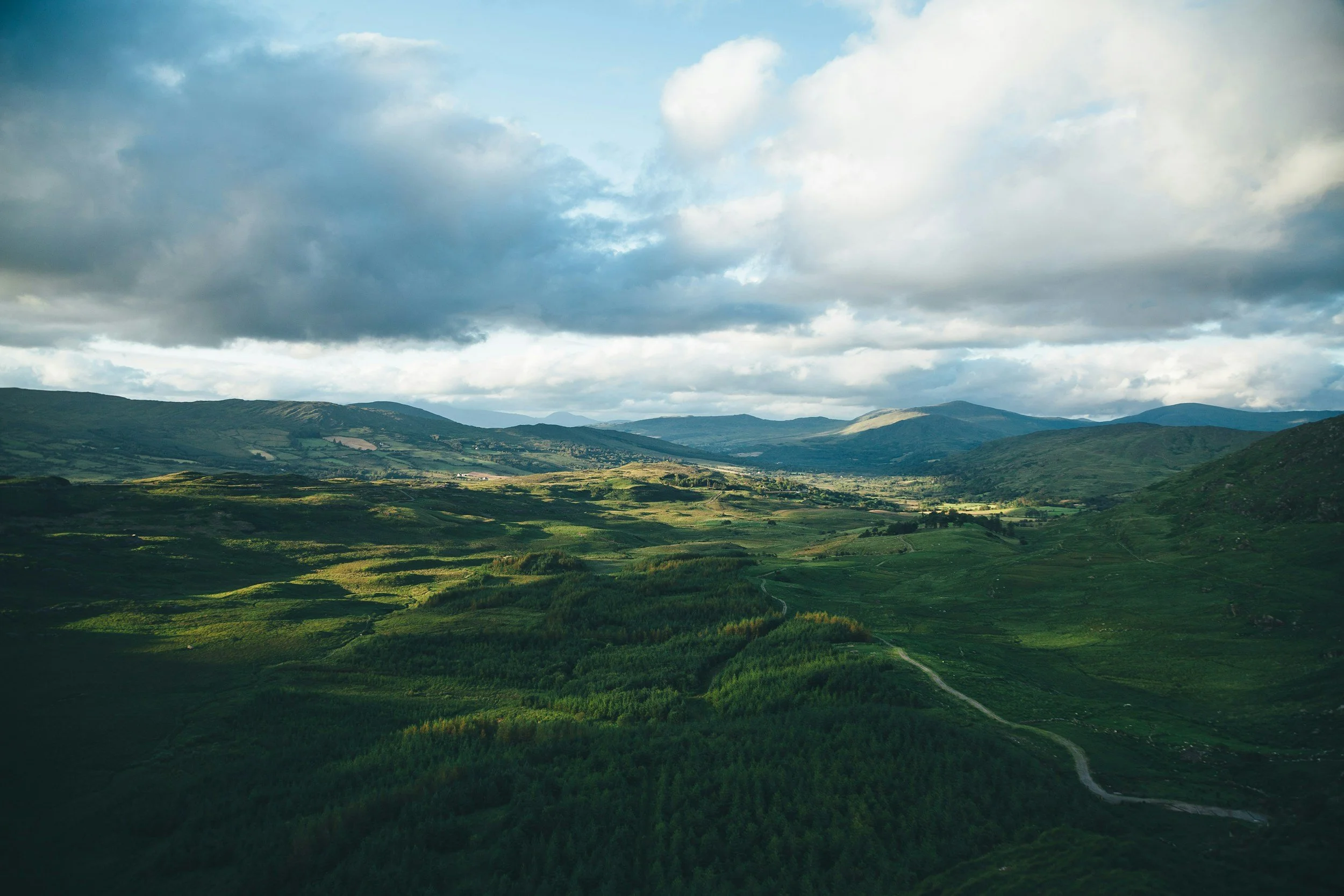 Scenic view of rolling green hills and mountains with partly cloudy sky overhead.