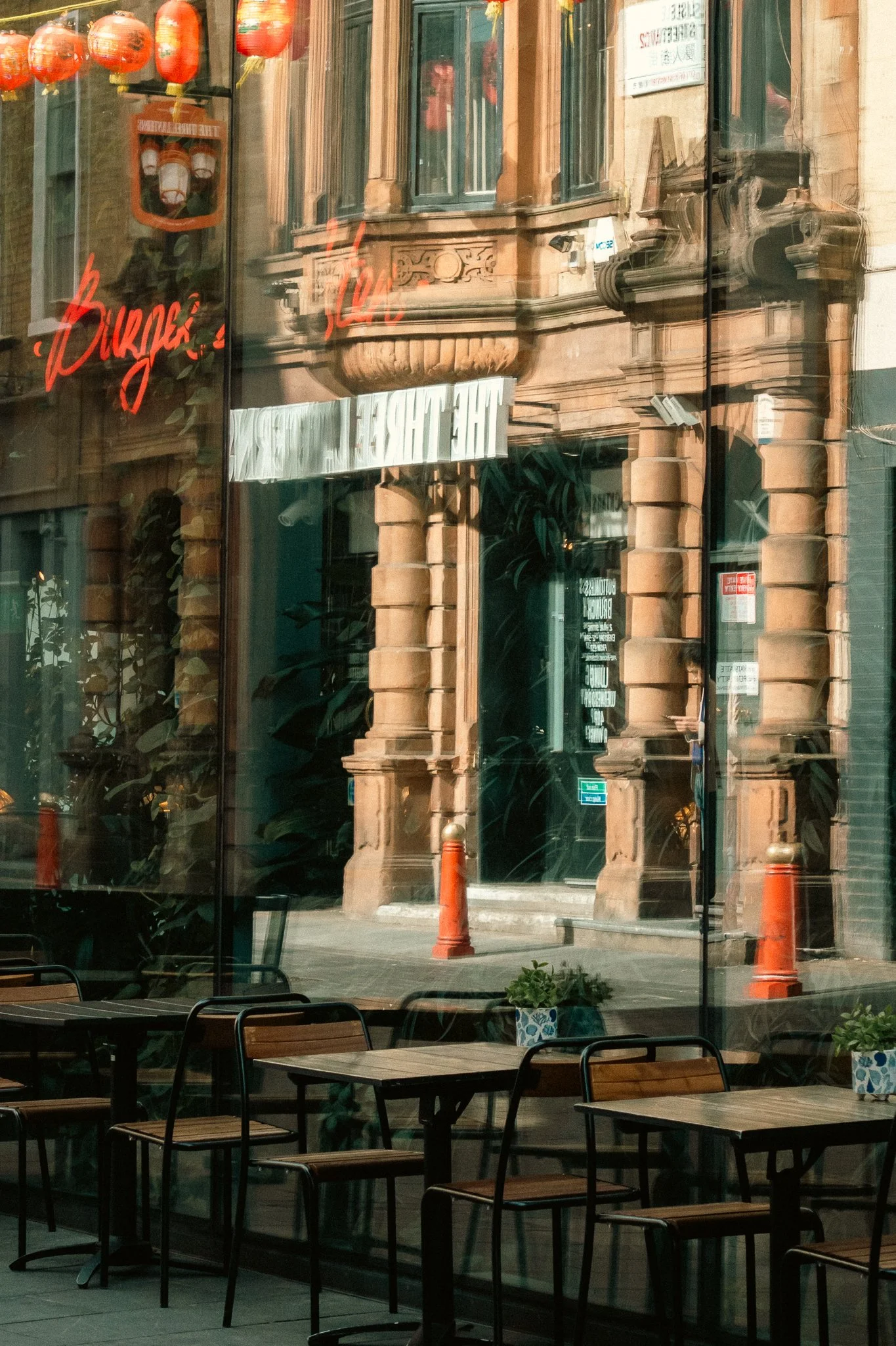 The image shows an outdoor view of a building with decorative stone architectural details and large green-framed windows. The reflection on the glass wall in front shows red Chinese lanterns and a sign that reads 