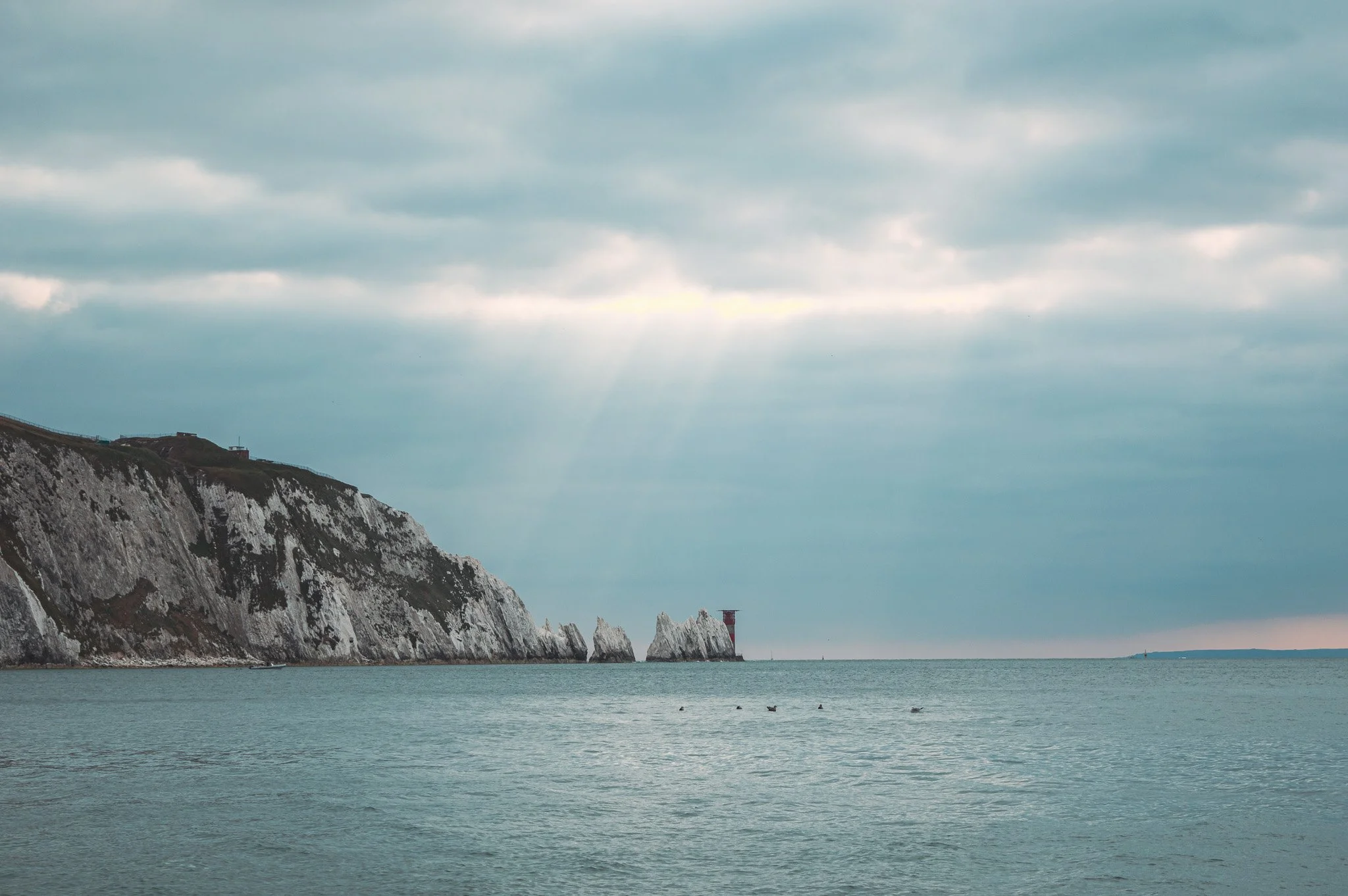 Cliffs along a coastline with a lighthouse in the distance under a cloudy sky.