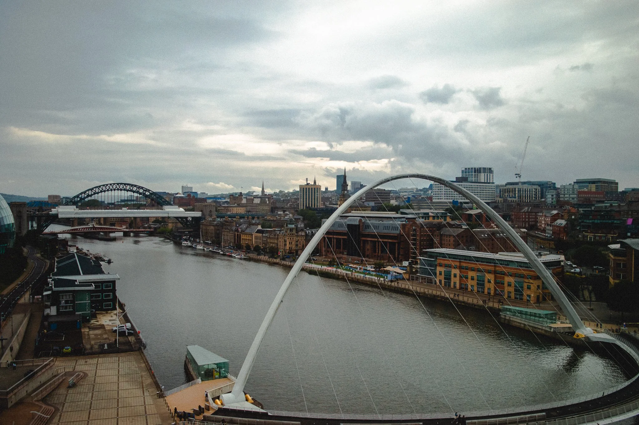 City skyline with river, bridge, and observation wheel under cloudy sky.