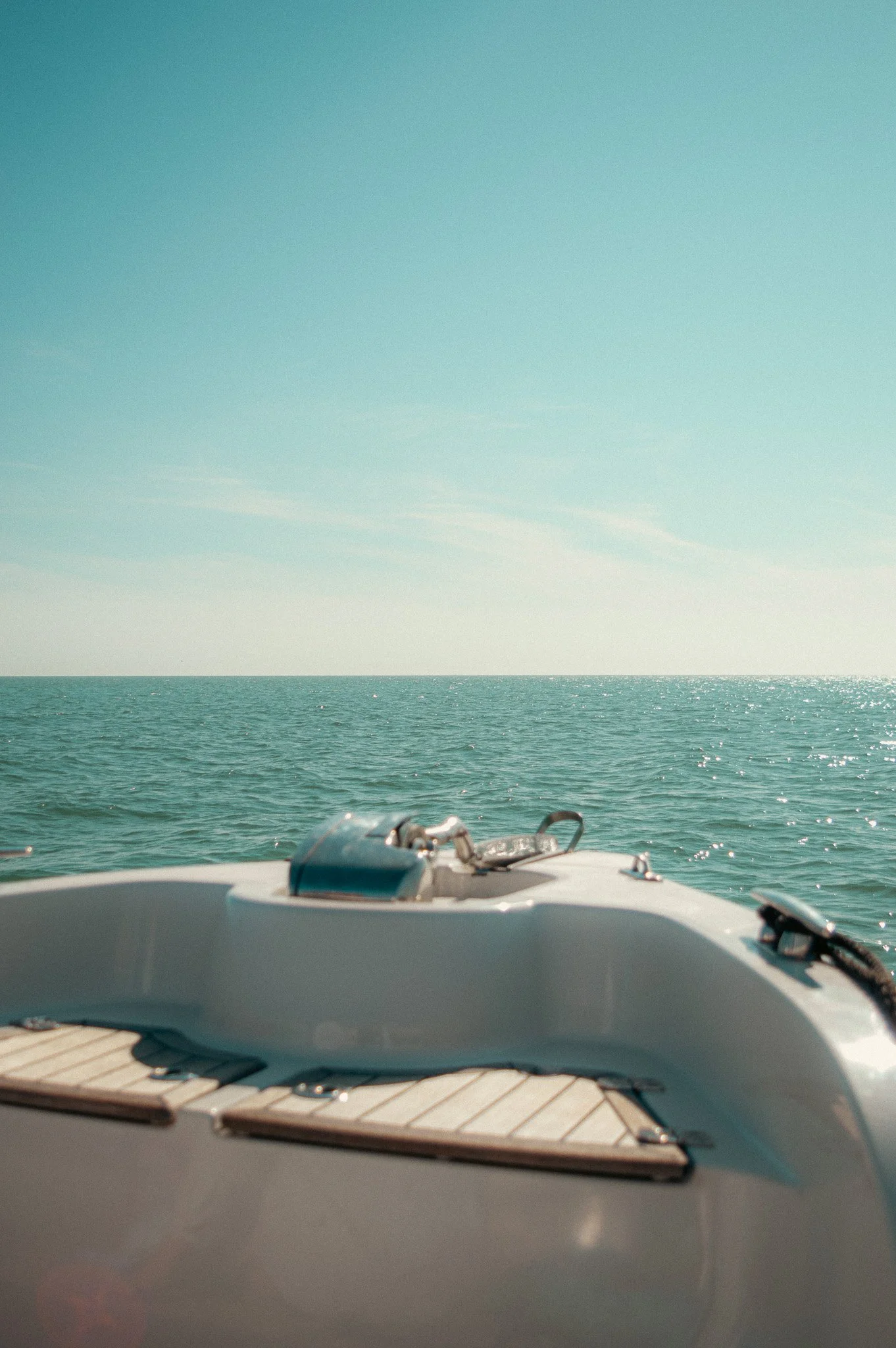 View from a boat showing a calm ocean with clear sky and no land in sight, part of the boat's deck with some metal fixtures in the foreground.