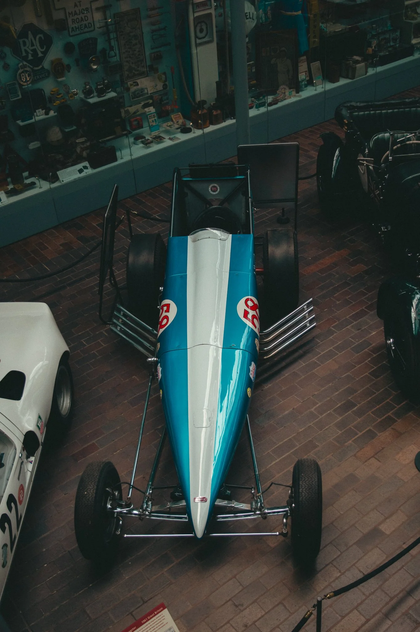 A vintage Formula 1 race car displayed in a museum, with a blue and white body and the number 50, surrounded by informational signs and other collectible items.