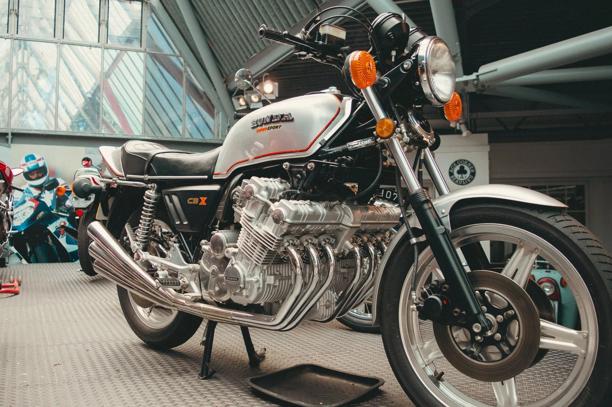 A Honda Super Sport motorcycle on a display stand in a showroom, with a helmet and posters of motorcycles in the background.