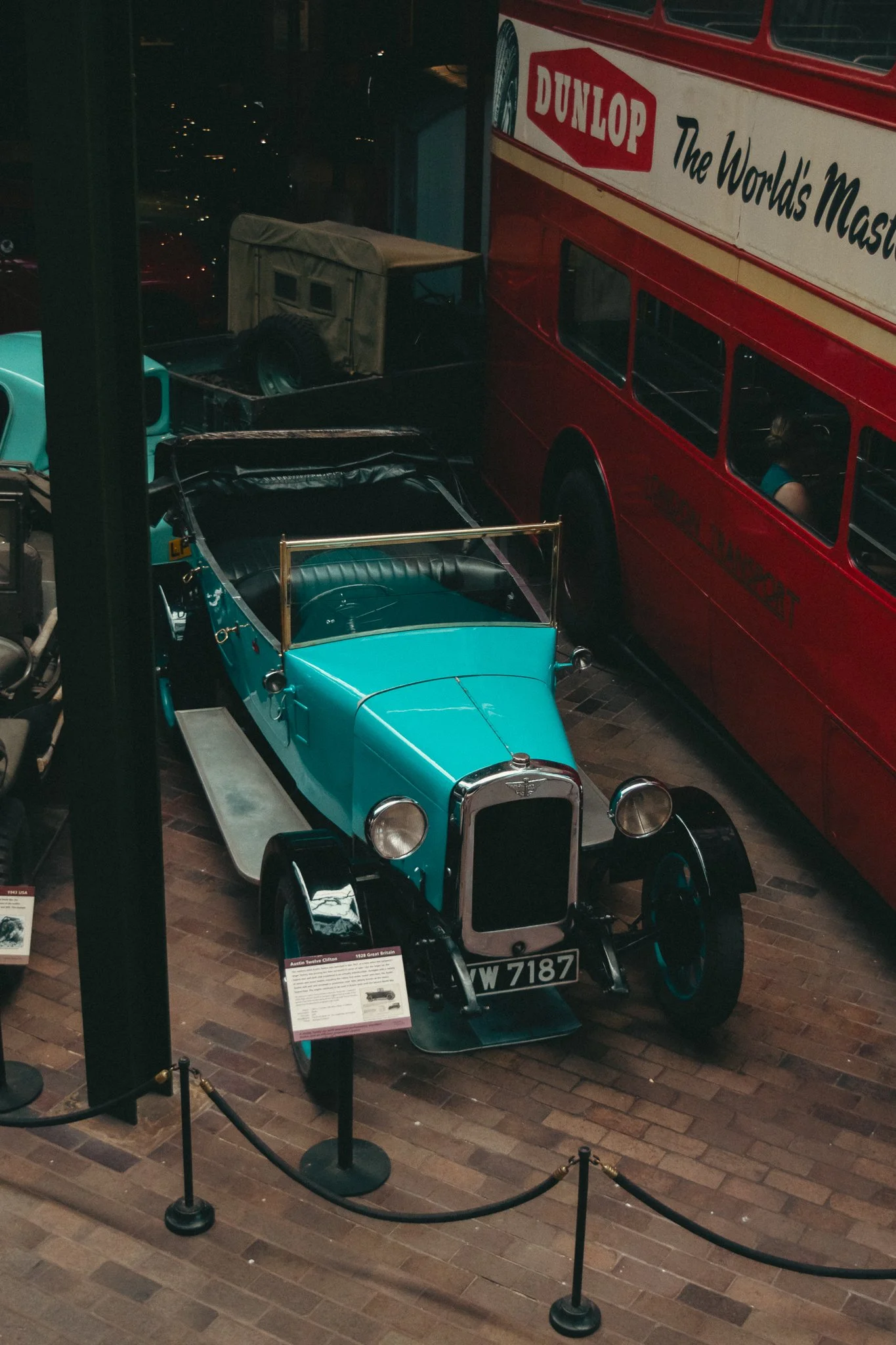A vintage blue car and an antique red bus displayed in a museum, with informational plaques and cordon barriers around them.