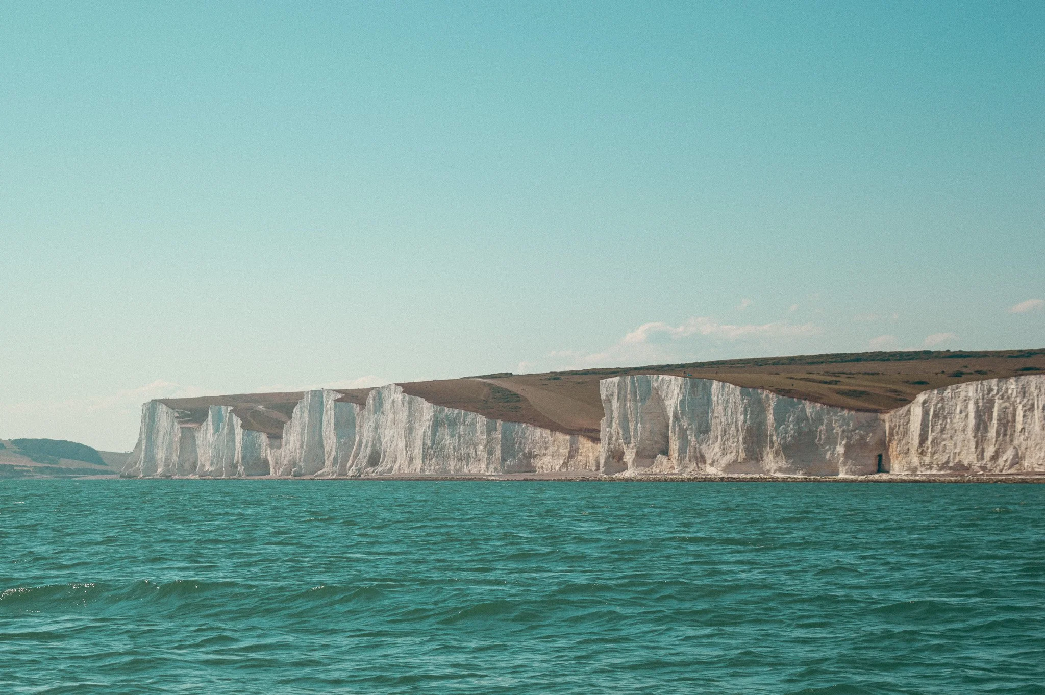 Cliffs of Dover along a body of water with a clear sky in the background.