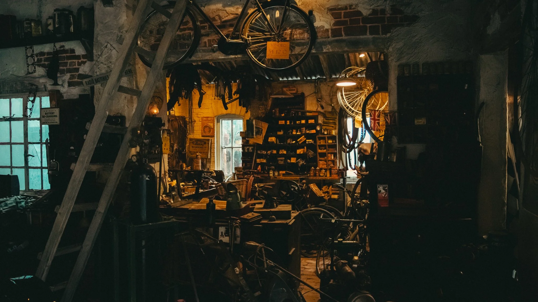 A dimly lit vintage bicycle and various tools hanging in a rustic workshop with brick walls and an open window.