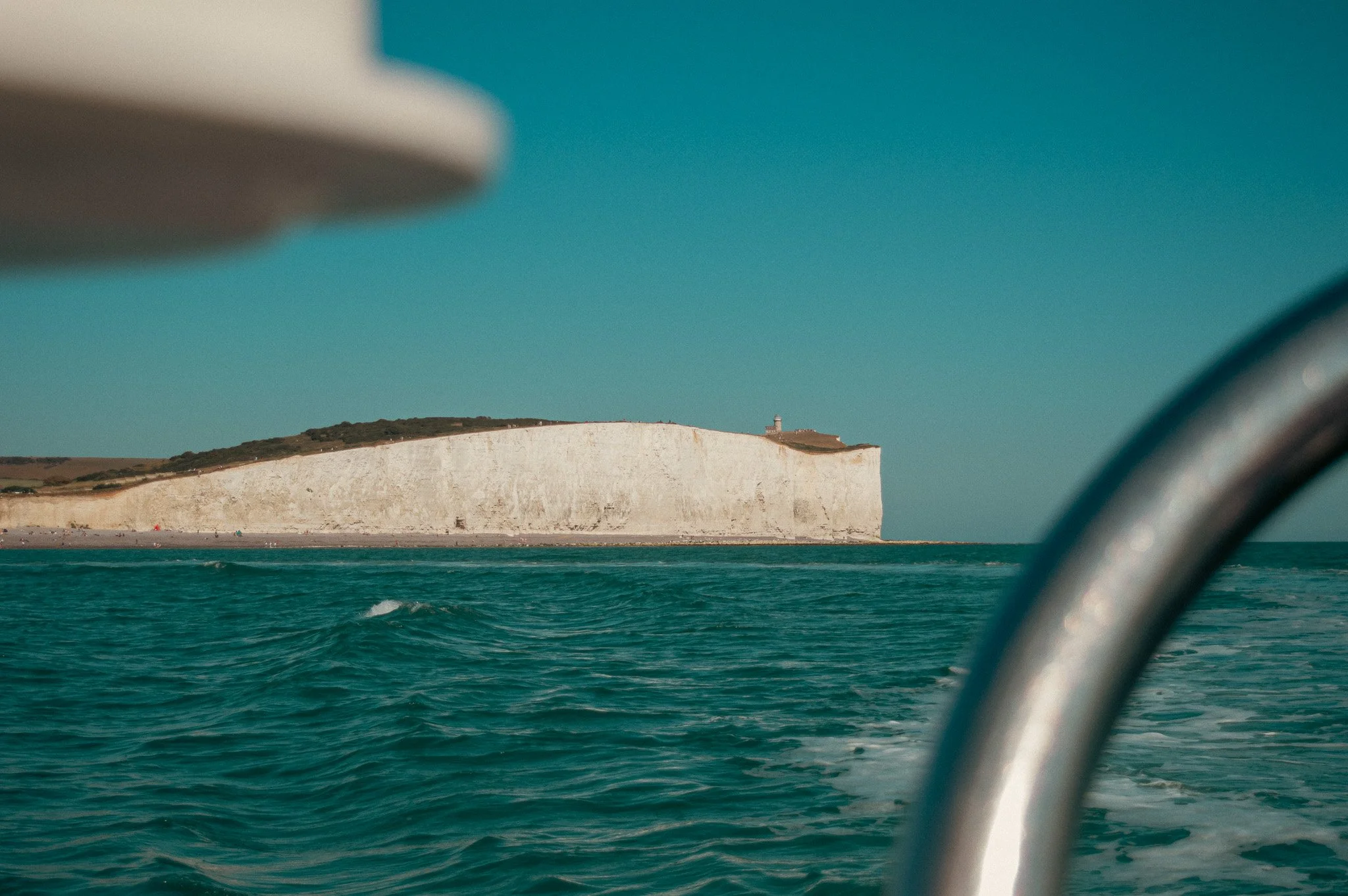 Photo of a white chalk cliff with a lighthouse on top, viewed through the window of a boat in the ocean.