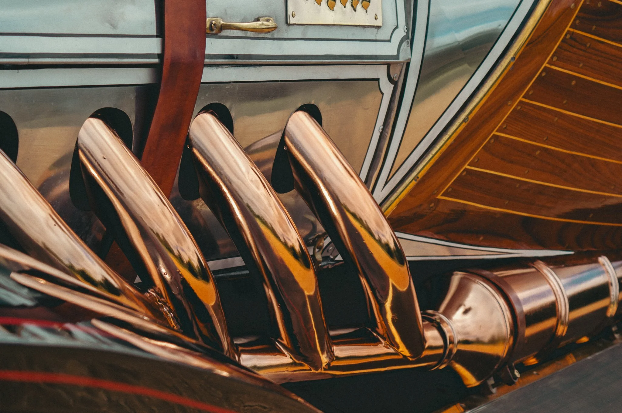Close-up view of polished brass musical instruments, possibly trumpets, lined up side by side on a wooden surface.