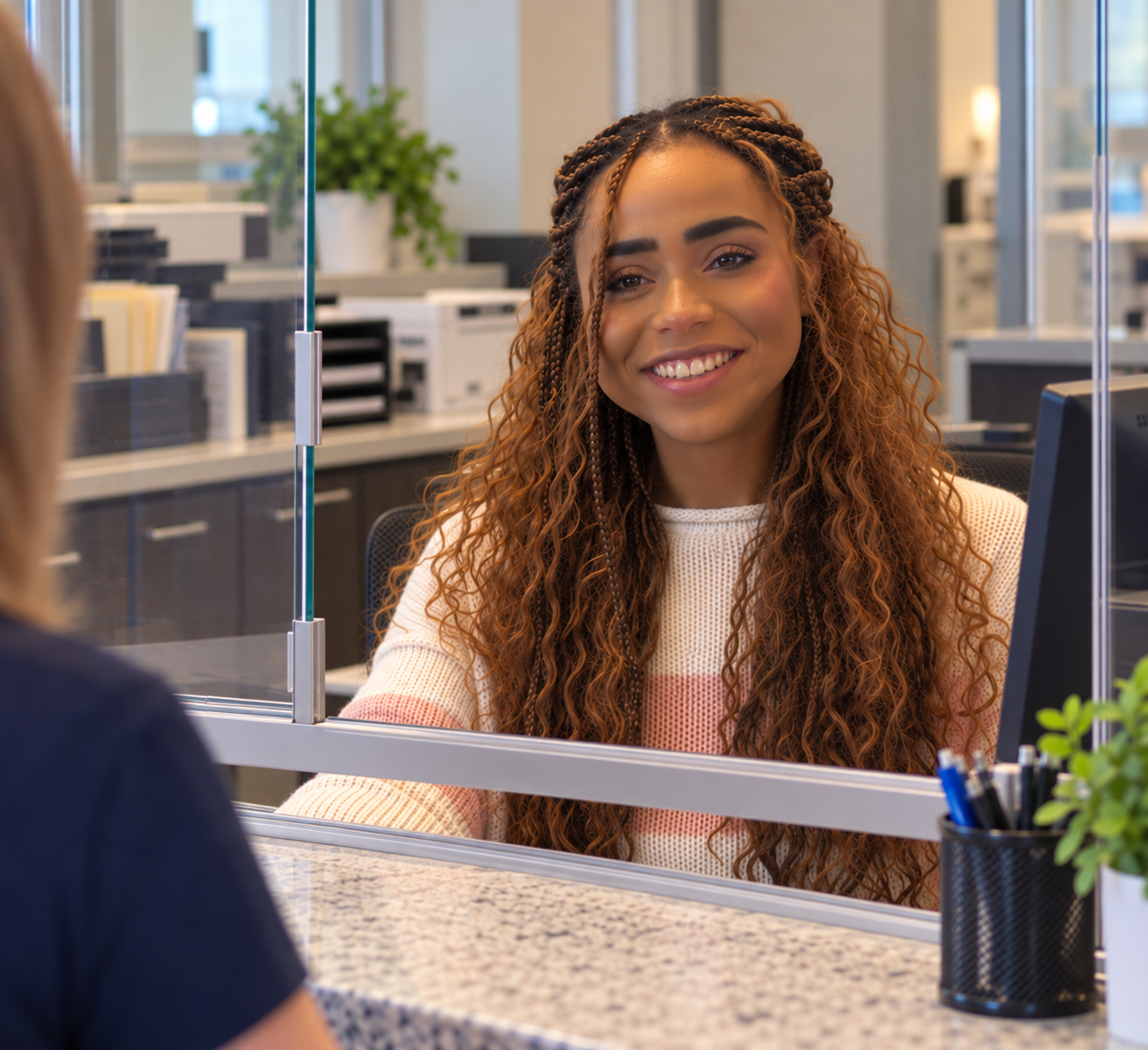Young woman with curly hair smiling at a bank teller across a counter.