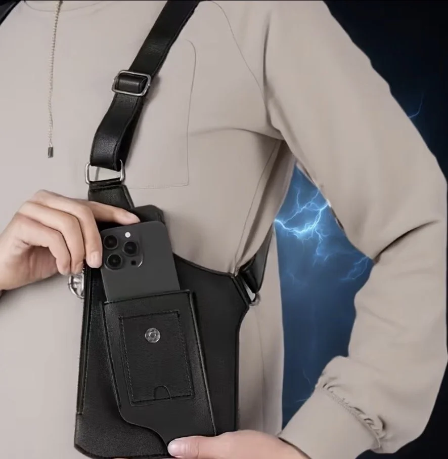 Person wearing a beige jacket with a black shoulder holster holding a smartphone in a pouch.