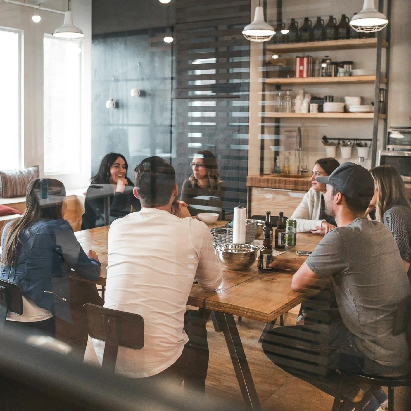 Groupe de personnes assises autour d'une table en bois dans un café, discutant et souriant.