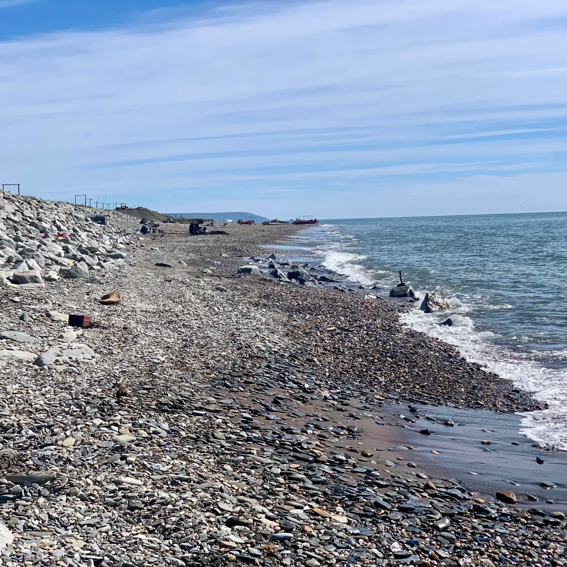 A sea glass hunting beach in Nome, Alaska, with people fishing and boats docked near the shore.