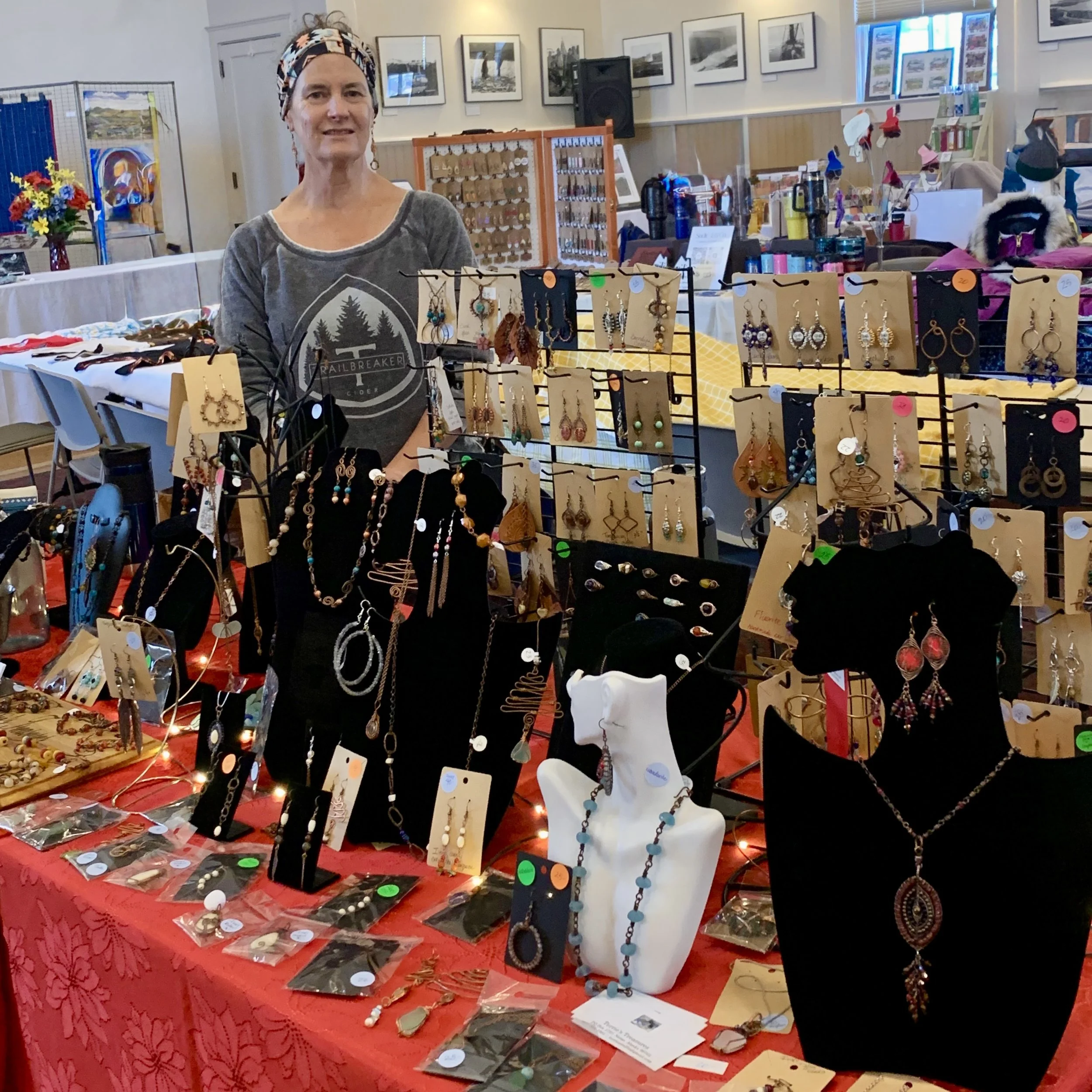 Terrie standing behind her table at a craft fair, displaying earrings, necklaces, and jewelry accessories.