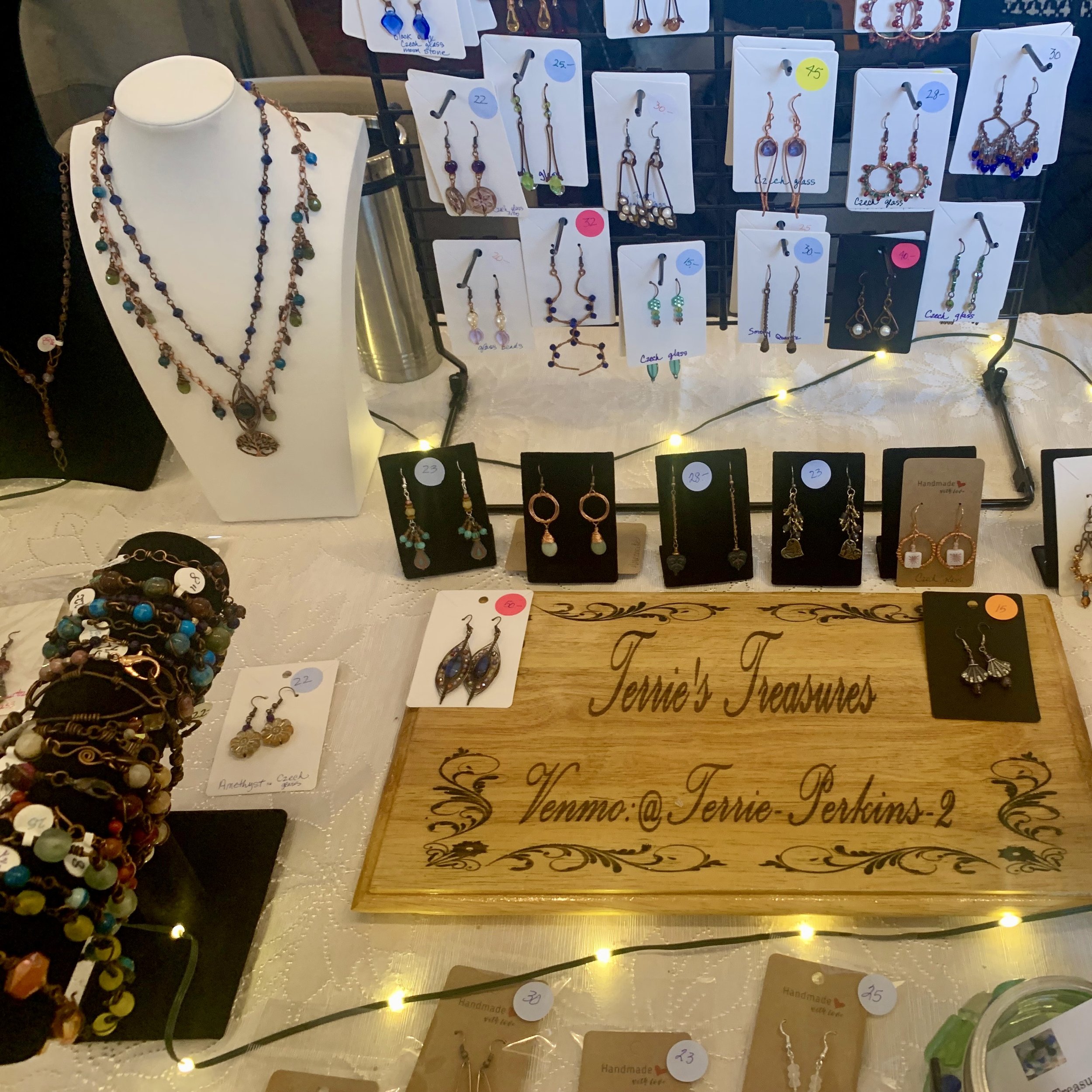 Display of handmade jewelry, including necklaces and earrings, arranged on white and black cards at a market stall. The jewelry features various beads and designs, with price tags attached.