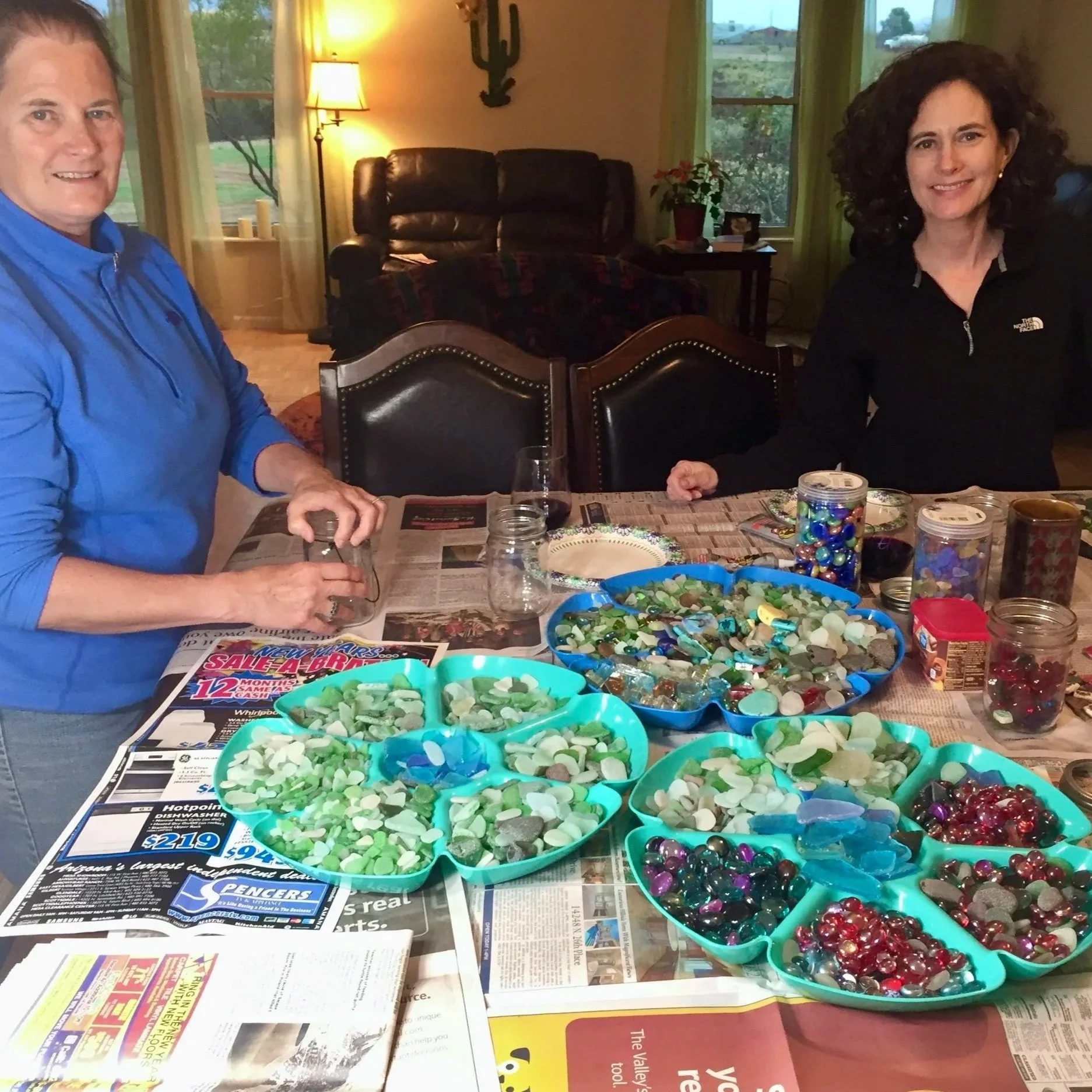 Terrie and her sister smiling on either side of a table covered with jewelry-making supplies in bowls.