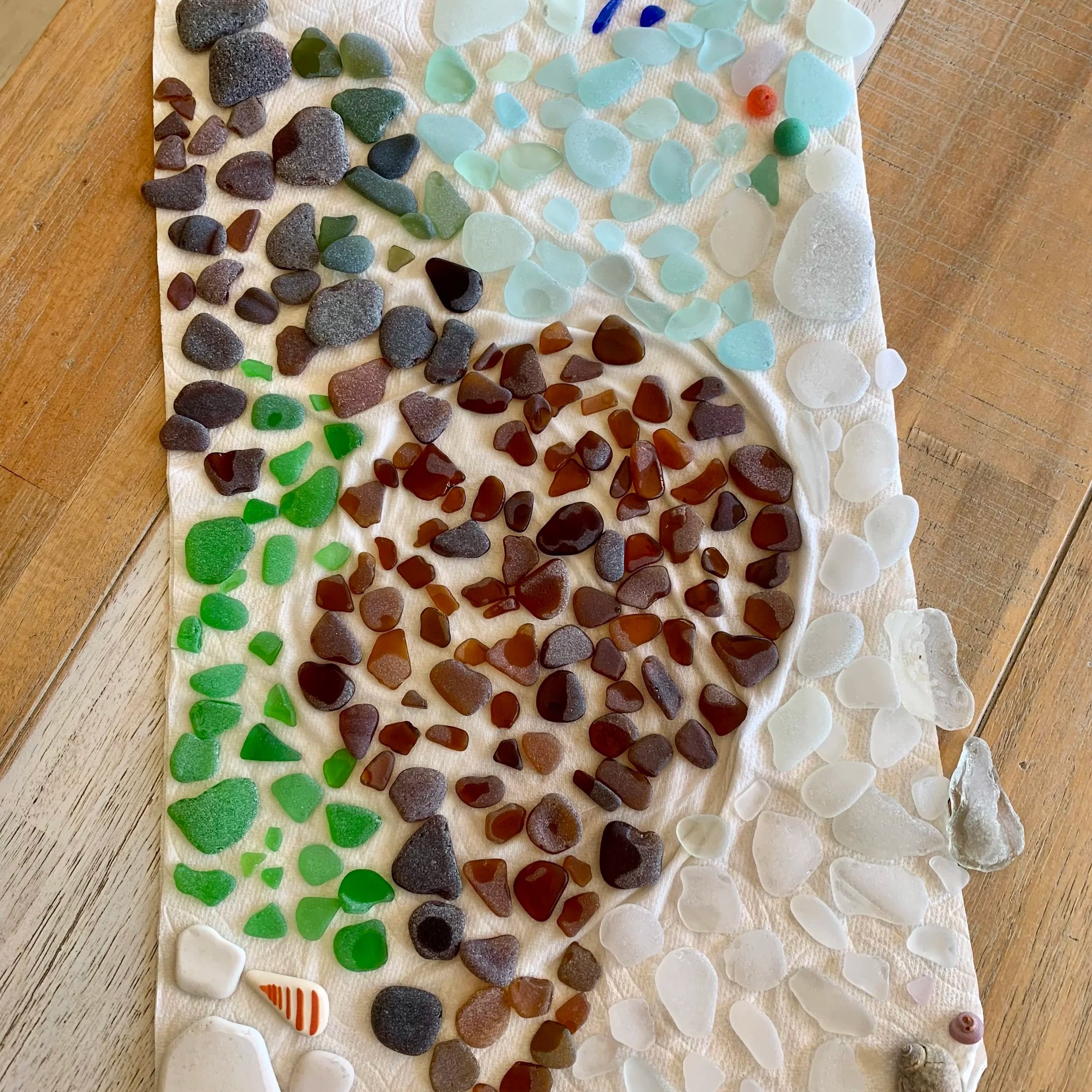 Sea glass and rocks in white, green, brown, blue, and amber arranged on a white paper towel.