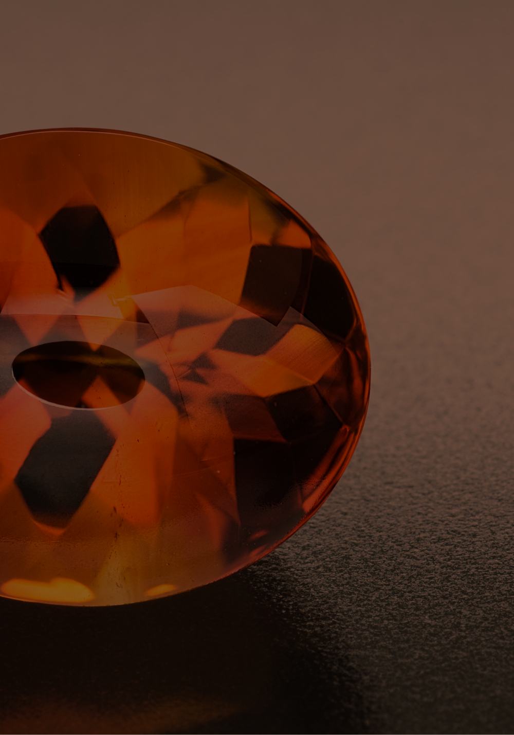 Nahaufnahme eines orangefarbenen, transparenten Kristalls in Form eines Fußballs auf einer dunklen Oberfläche.