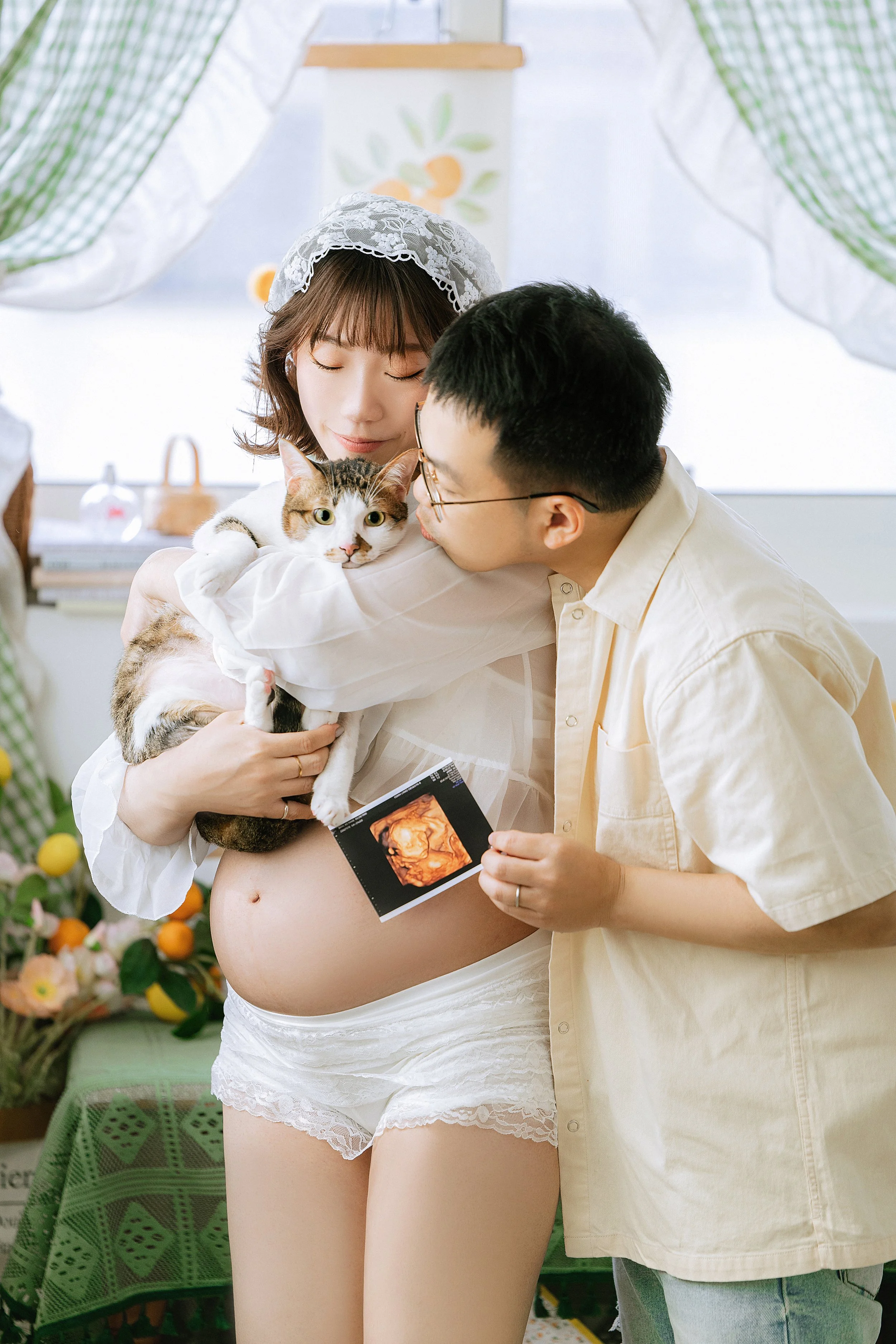 爸爸抱著懷孕的孕婦，孕婦抱著貓咪一起拍攝全家福