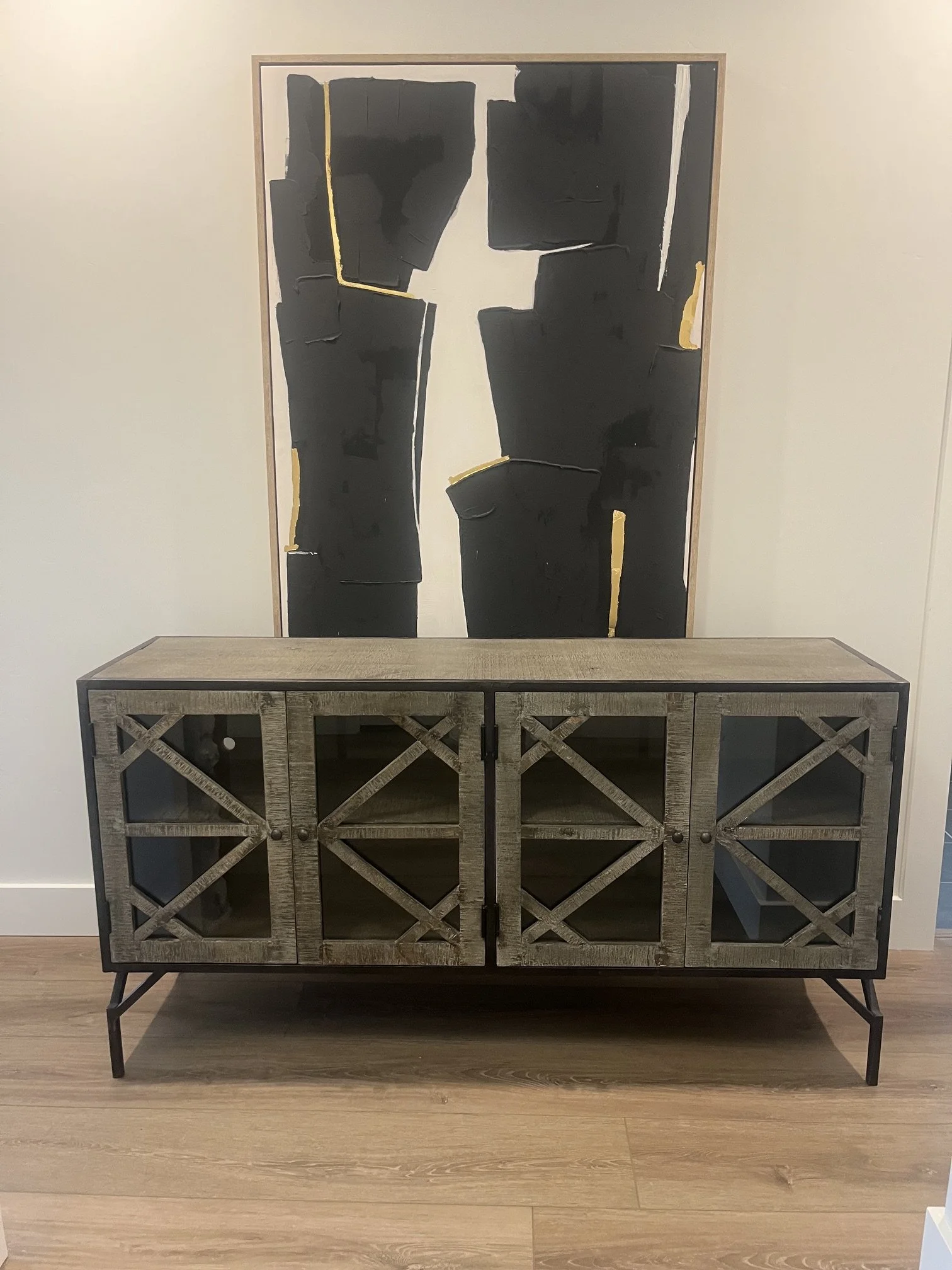 Modern console cabinet beneath black and gold abstract artwork, an example of an item sold by Tapie Takes Care of It.