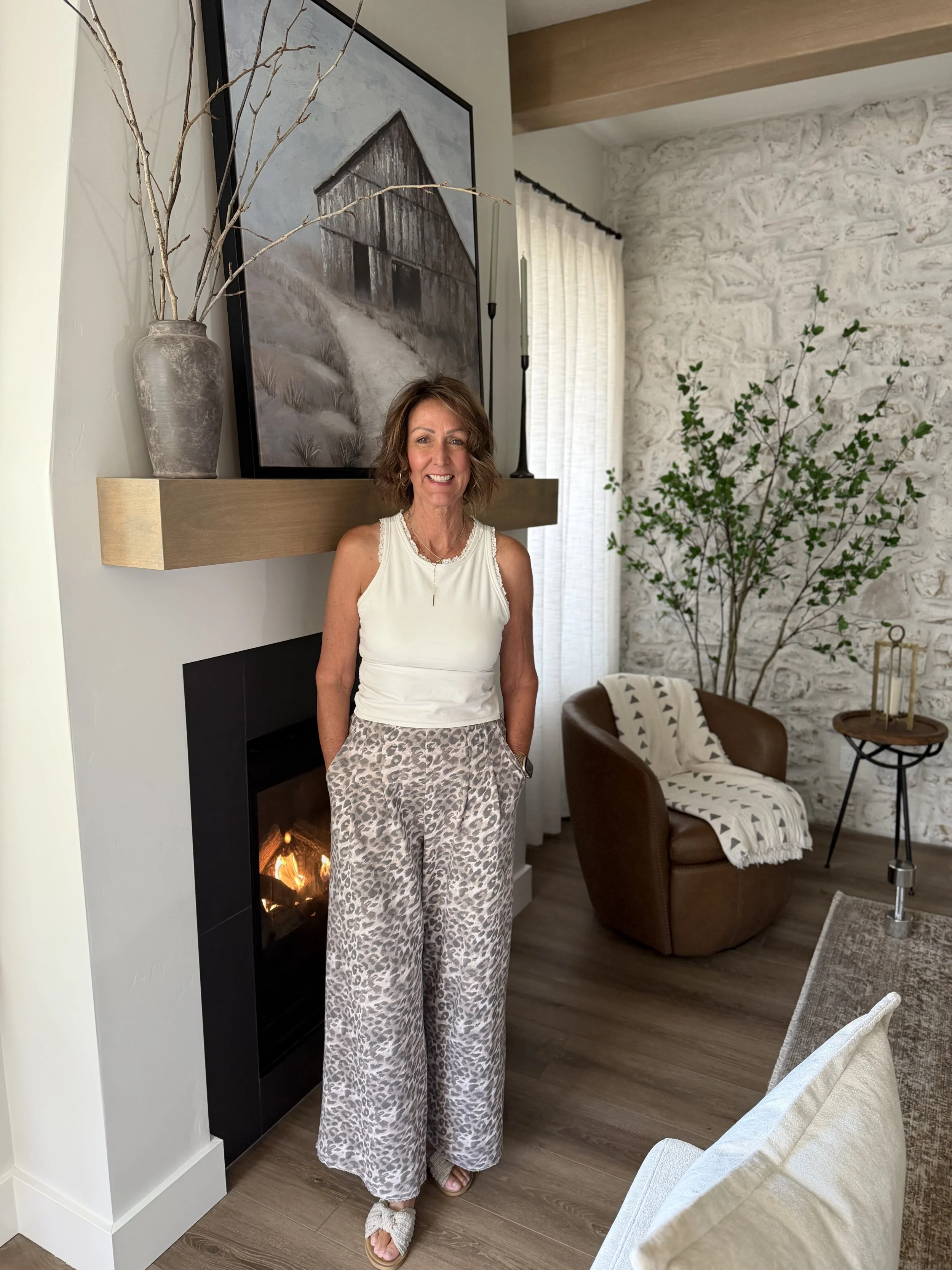 Full-length portrait of Marlene Tapie standing beside a fireplace, with her complete outfit and sandals visible.