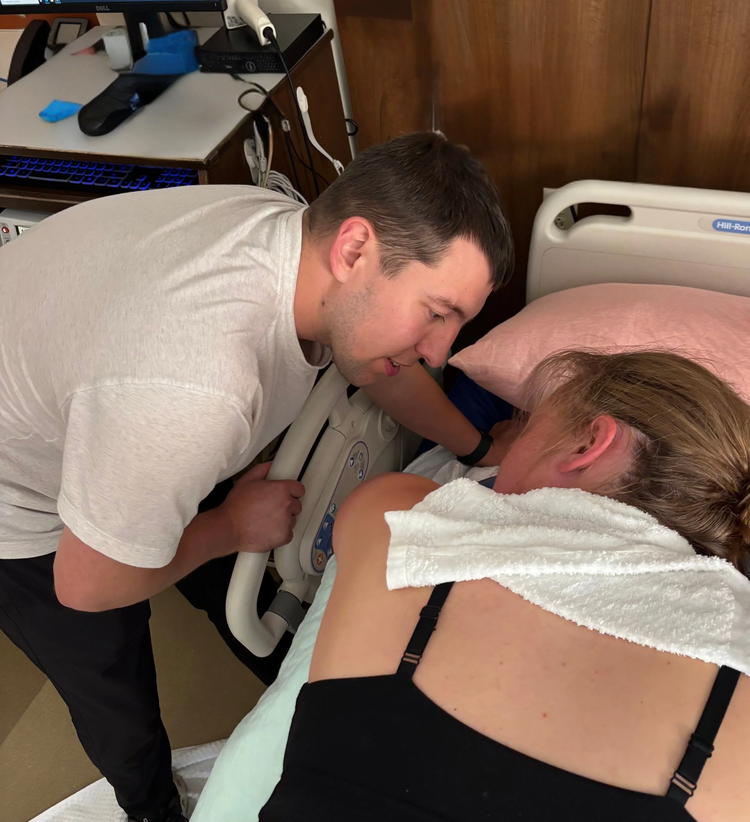 A man performing CPR on a woman lying on a hospital bed, with medical equipment nearby.