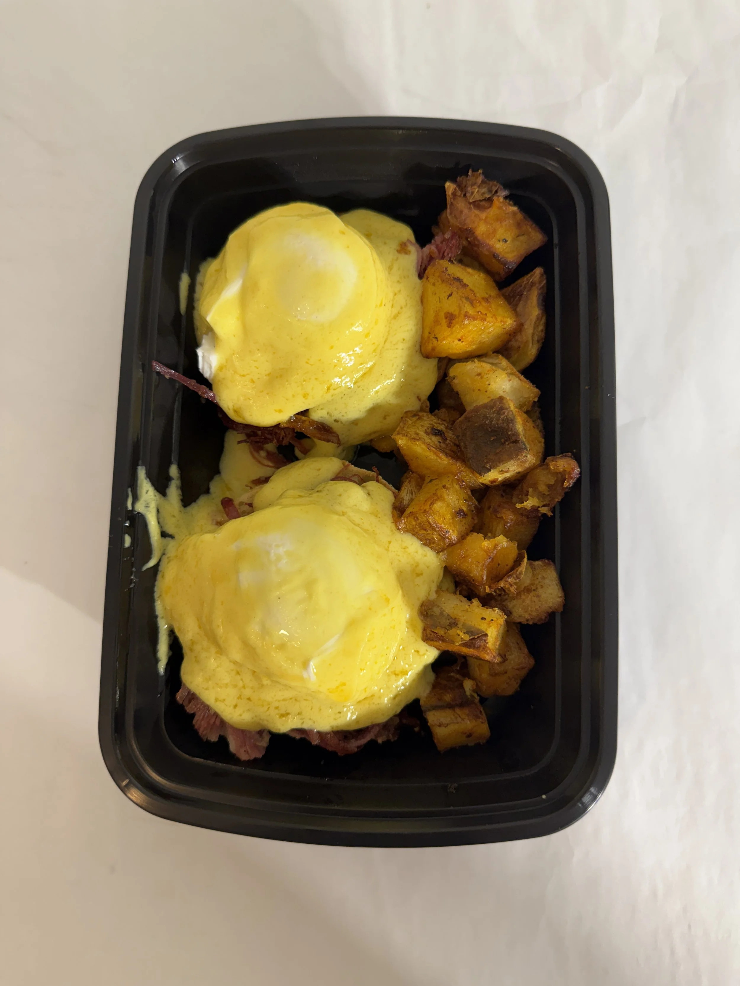 Eggs Benedict with hollandaise and roasted breakfast potatoes in a takeout container from Royal Diner