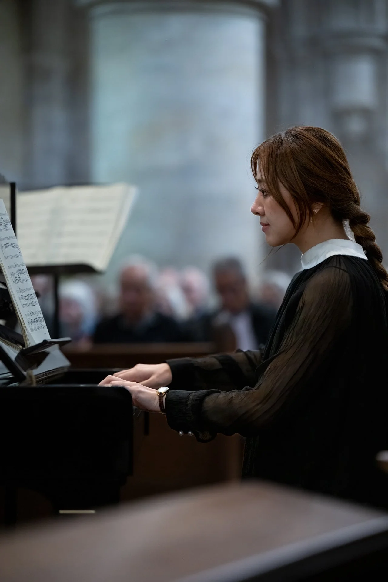 A woman playing a piano during a formal concert with an orchestra in the background.