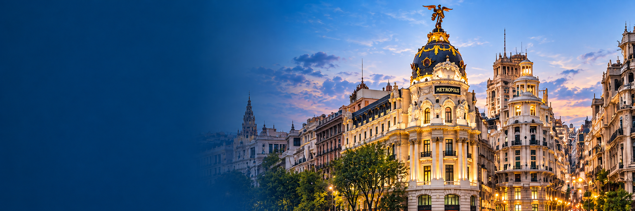 Photo of the Metropolis building in Madrid, Spain, at sunset, with its ornate architecture and a golden statue on top, illuminated against a blue sky with clouds.