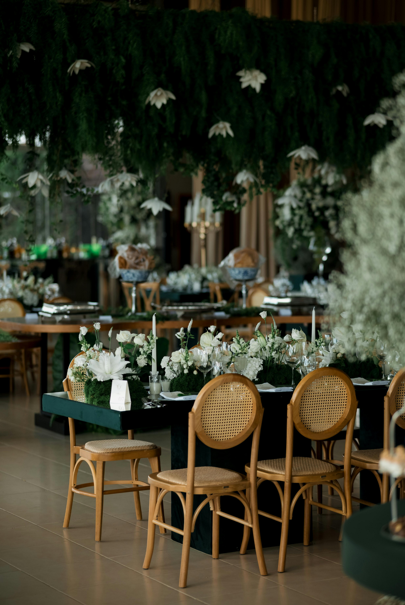 Elegant indoor event space decorated with white flowers, greenery, candles, and neatly arranged tables and chairs for a celebration, gathering, product launch, press and/or beauty day