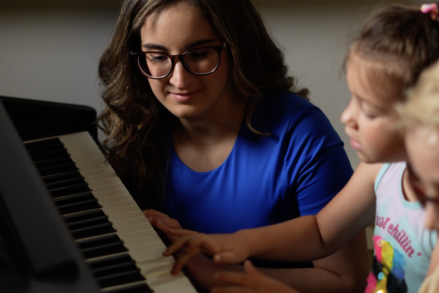 Adult woman teaching young girl to play piano together.