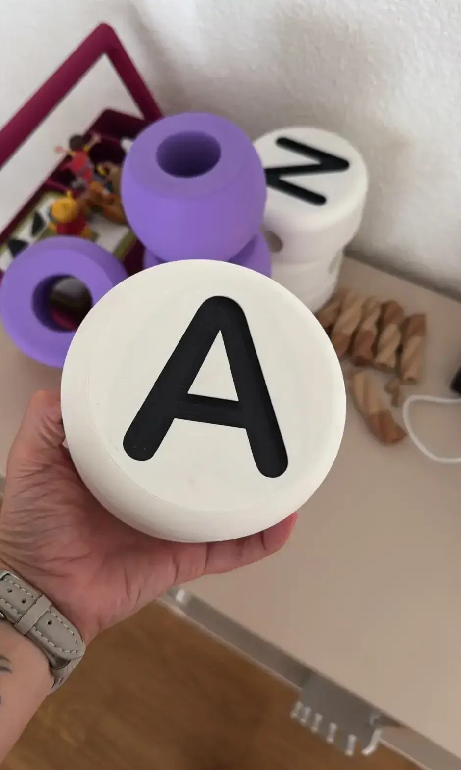 Hand hält eine grosse 3D-gedruckte Buchstabenperle «A» vor weiteren XXL-Perlen