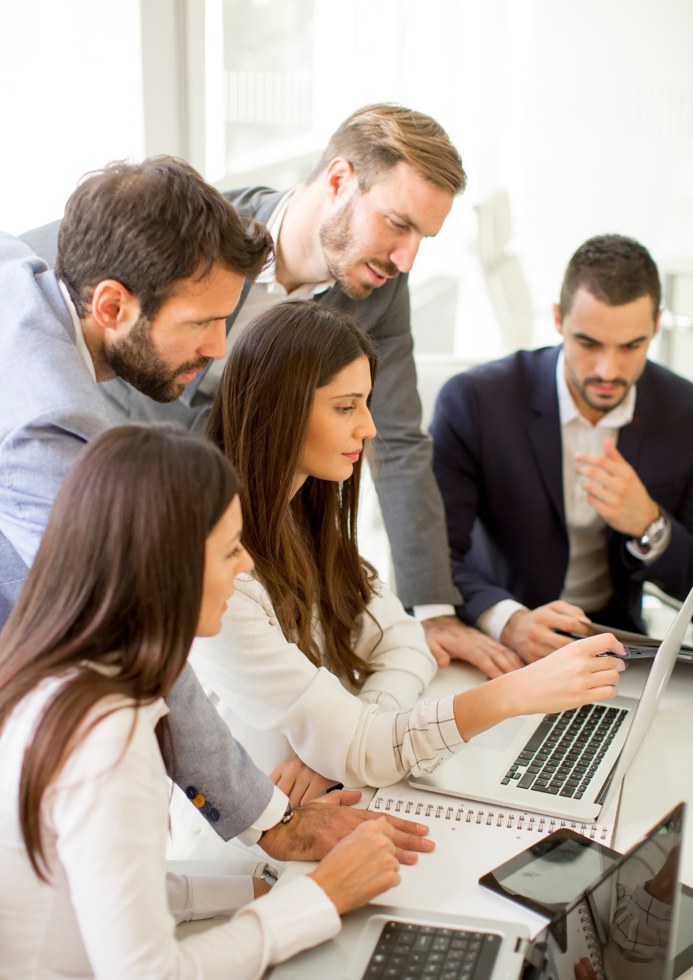 Businesspeople working around a laptop in a meeting or office setting.