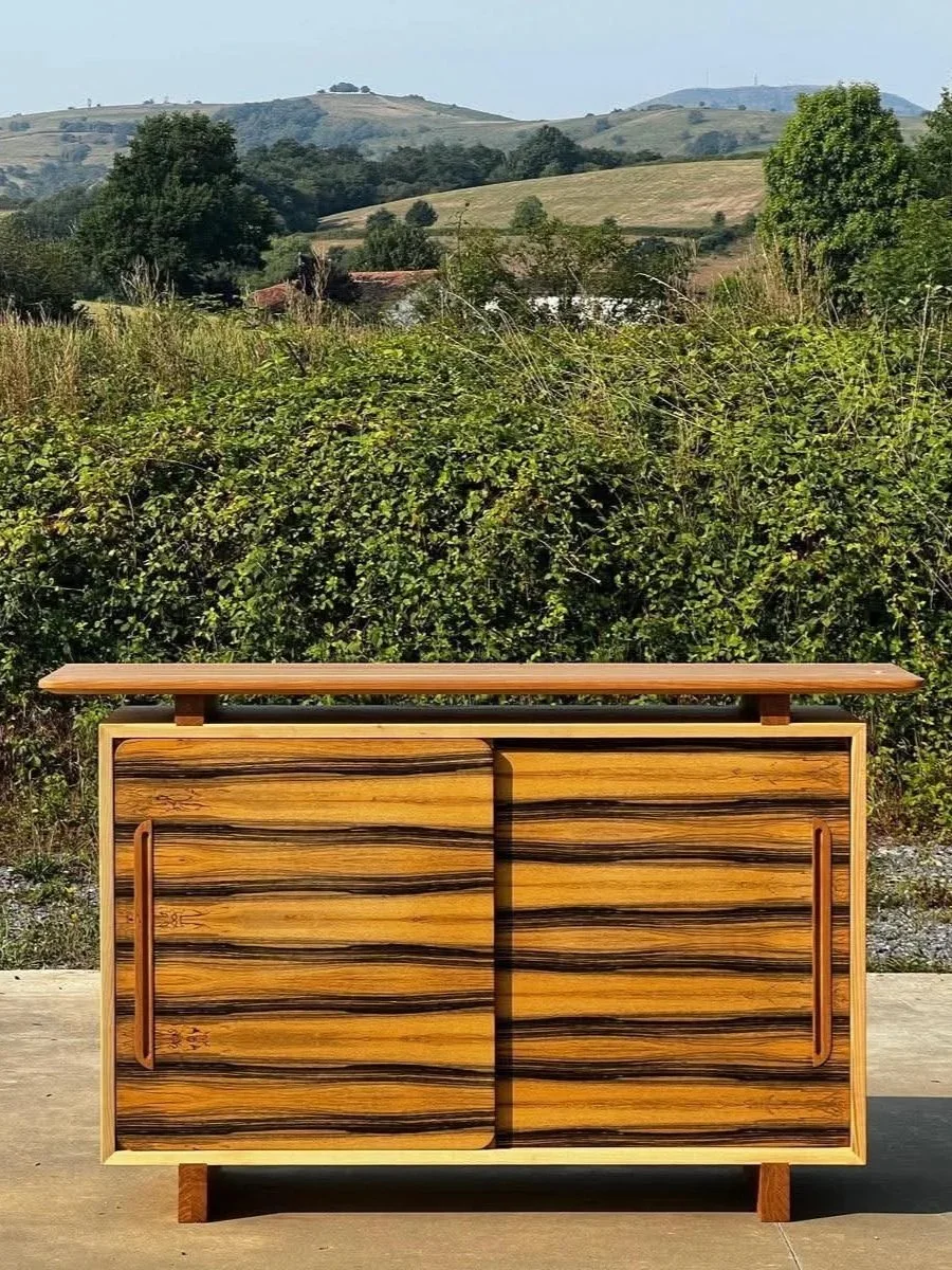 meuble en bois avec deux portes coulissantes, placé à l'extérieur sur une surface plane, avec un paysage de collines et d'arbres en arrière-plan