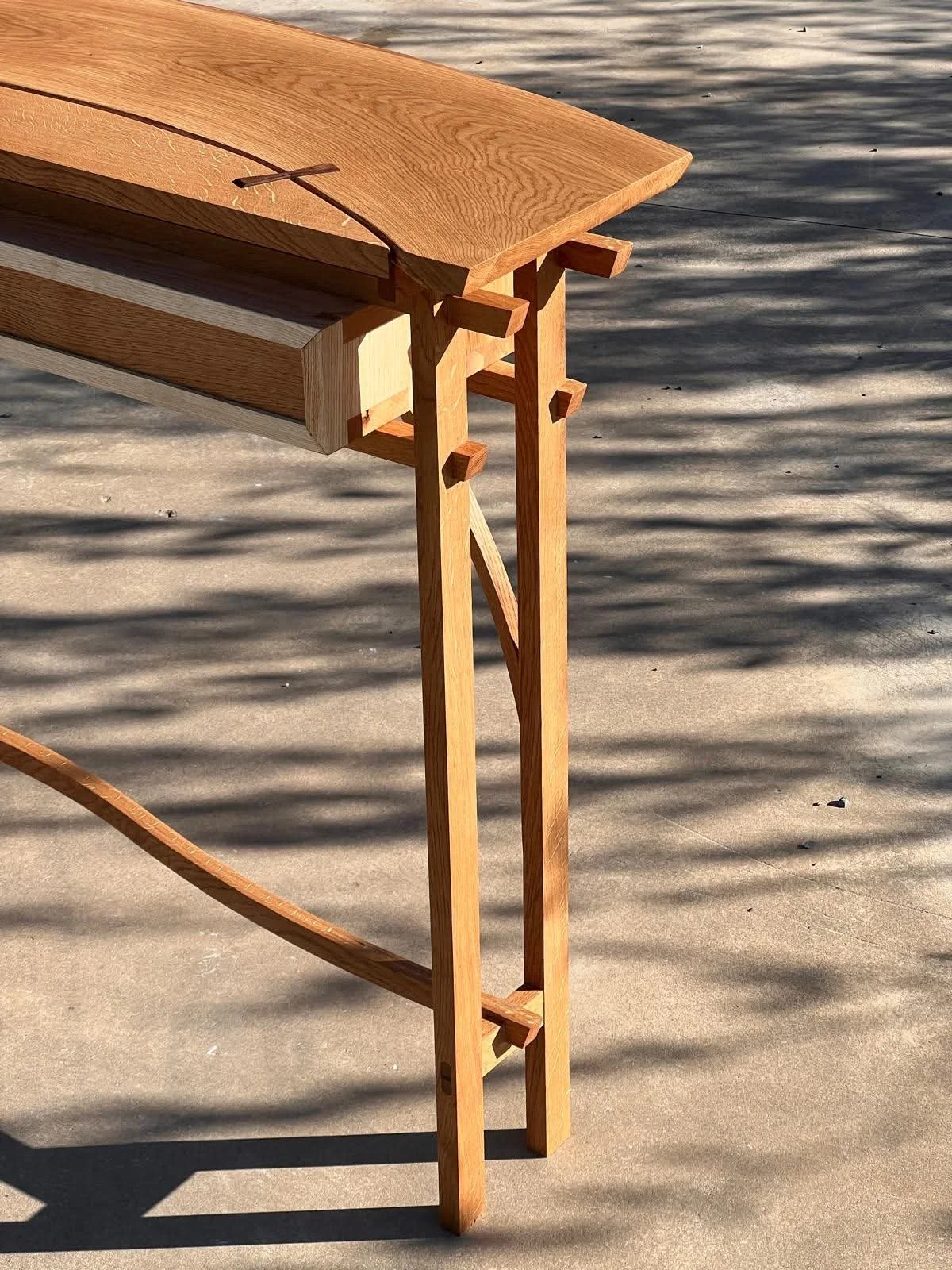 Table en bois en cours de fabrication, vue partielle, avec pied artistique en bois, éclairage naturel et ombres sur le sol.