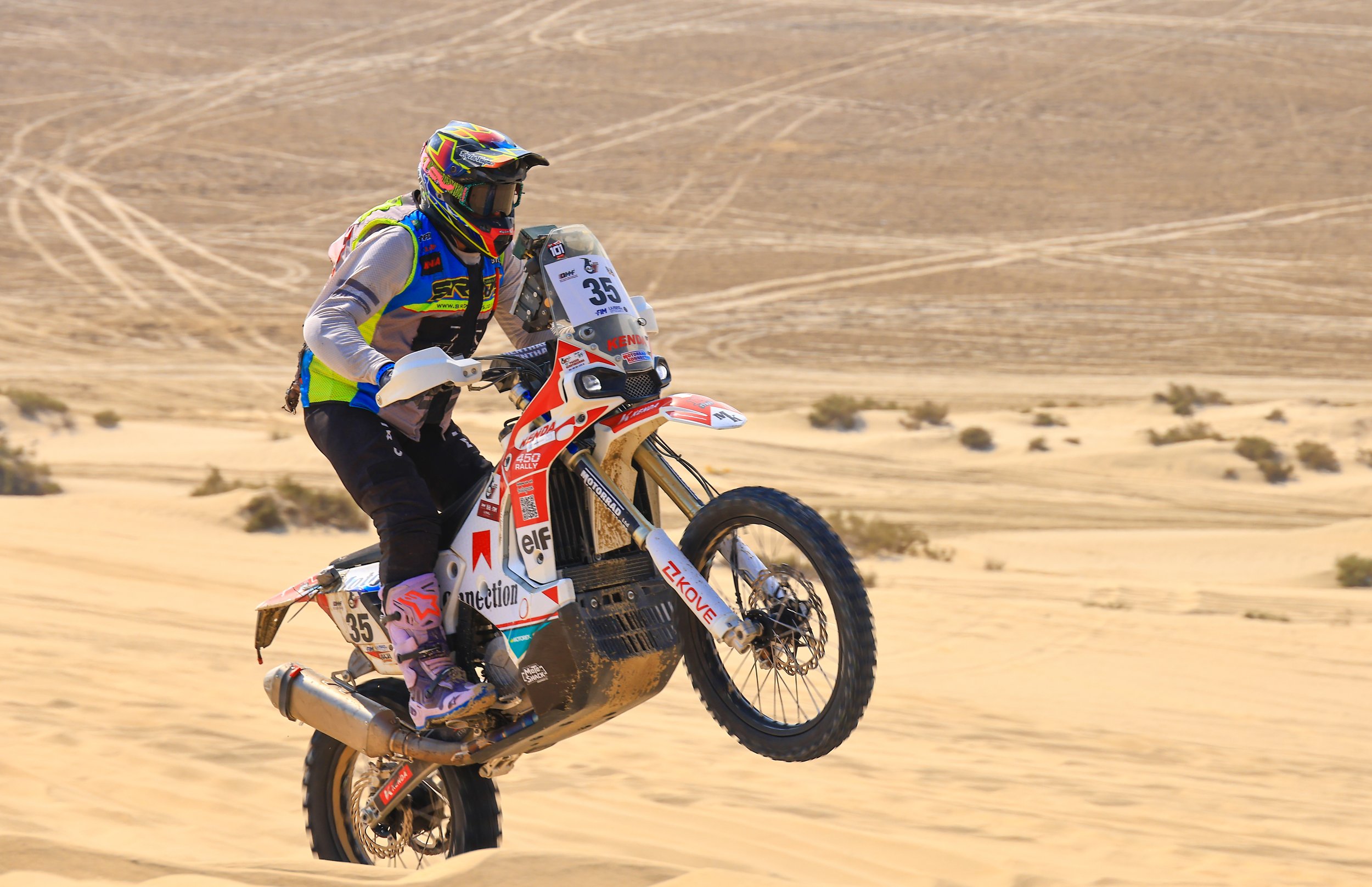 A motorcyclist riding a dirt bike through a sandy desert landscape.