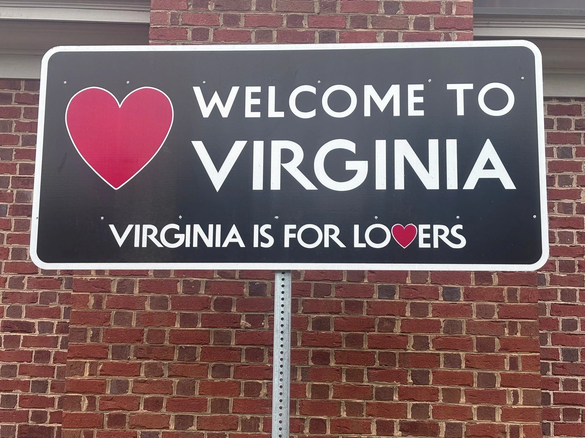Rectangular Welcome to Virginia sign contains heart and Virginia is for lovers slogan.