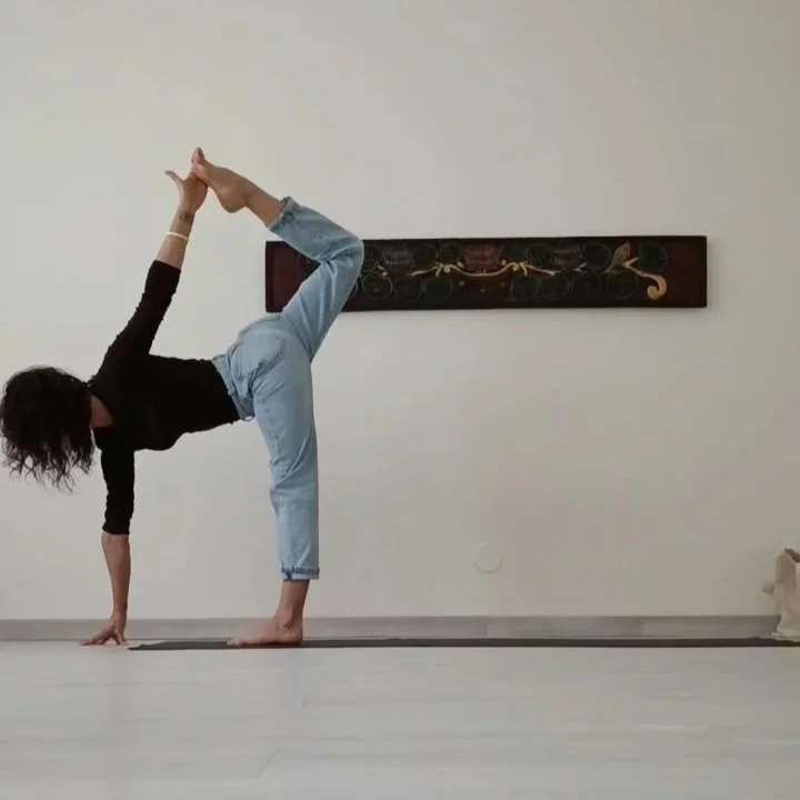 A woman performing a yoga pose in a room with a painting on the wall behind her.