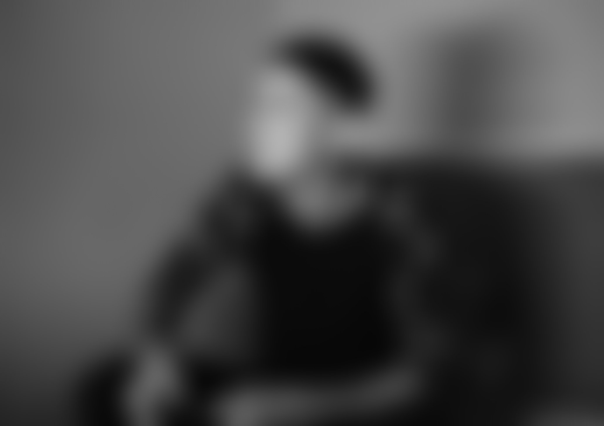 Blurred grayscale image with indistinct dark shapes and lighter background.