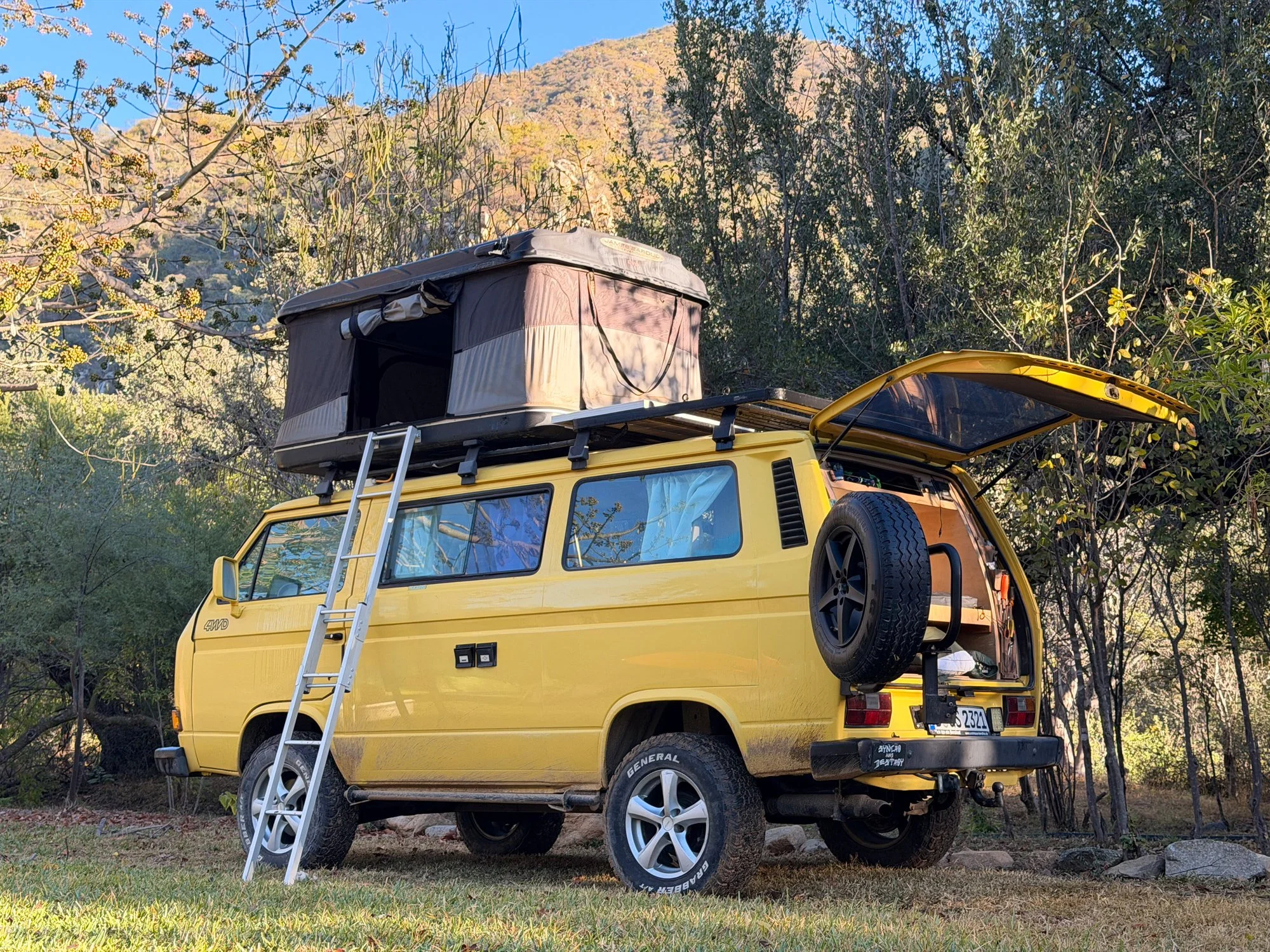 Yellow Volkswagen Syncro camper with its rooftop tent open at a woodland camp