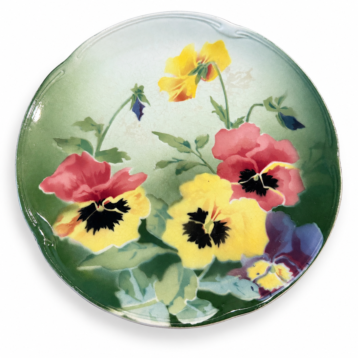 Angled view of the Lunéville pansy plate showing its molded rim and glaze crazing.