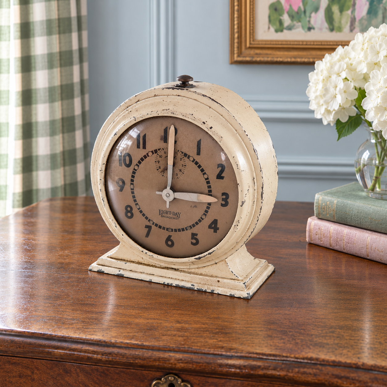 Angled view of the cream metal Broadcast clock showing its round case and stepped pedestal base.