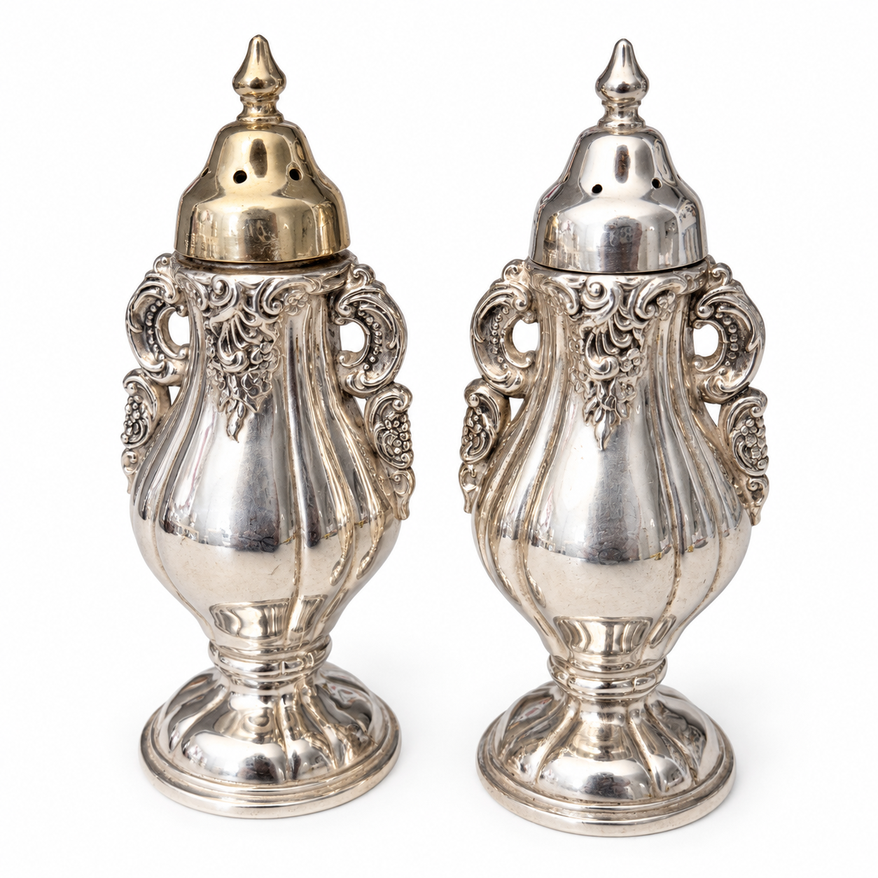 Pair of Wallace Baroque silverplate shakers with ornate scroll handles and pointed finials.