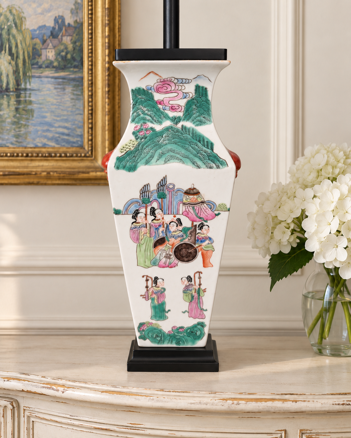 Figural porcelain lamp body on an ivory French console beside white hydrangeas.