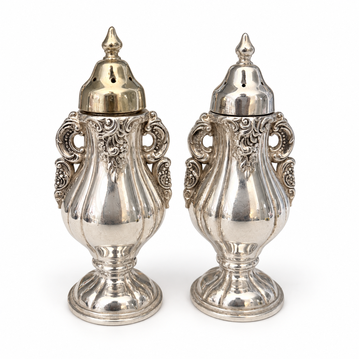 Front view of both Baroque shakers with pierced caps and reflective silverplate surfaces.