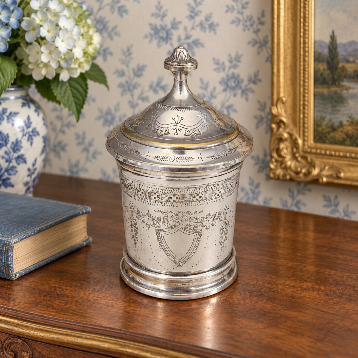 Silver-tone cylindrical jar with an engraved body, domed lid and tall finial.