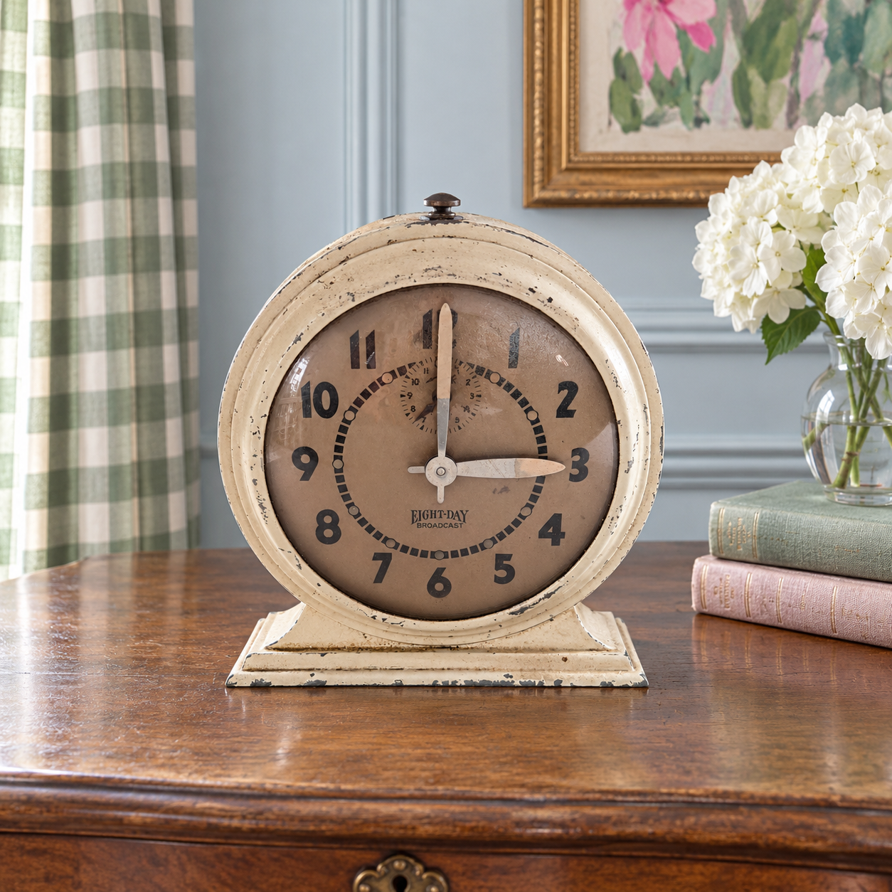 Cream Broadcast clock on a French writing desk with books and a green checked curtain behind it.