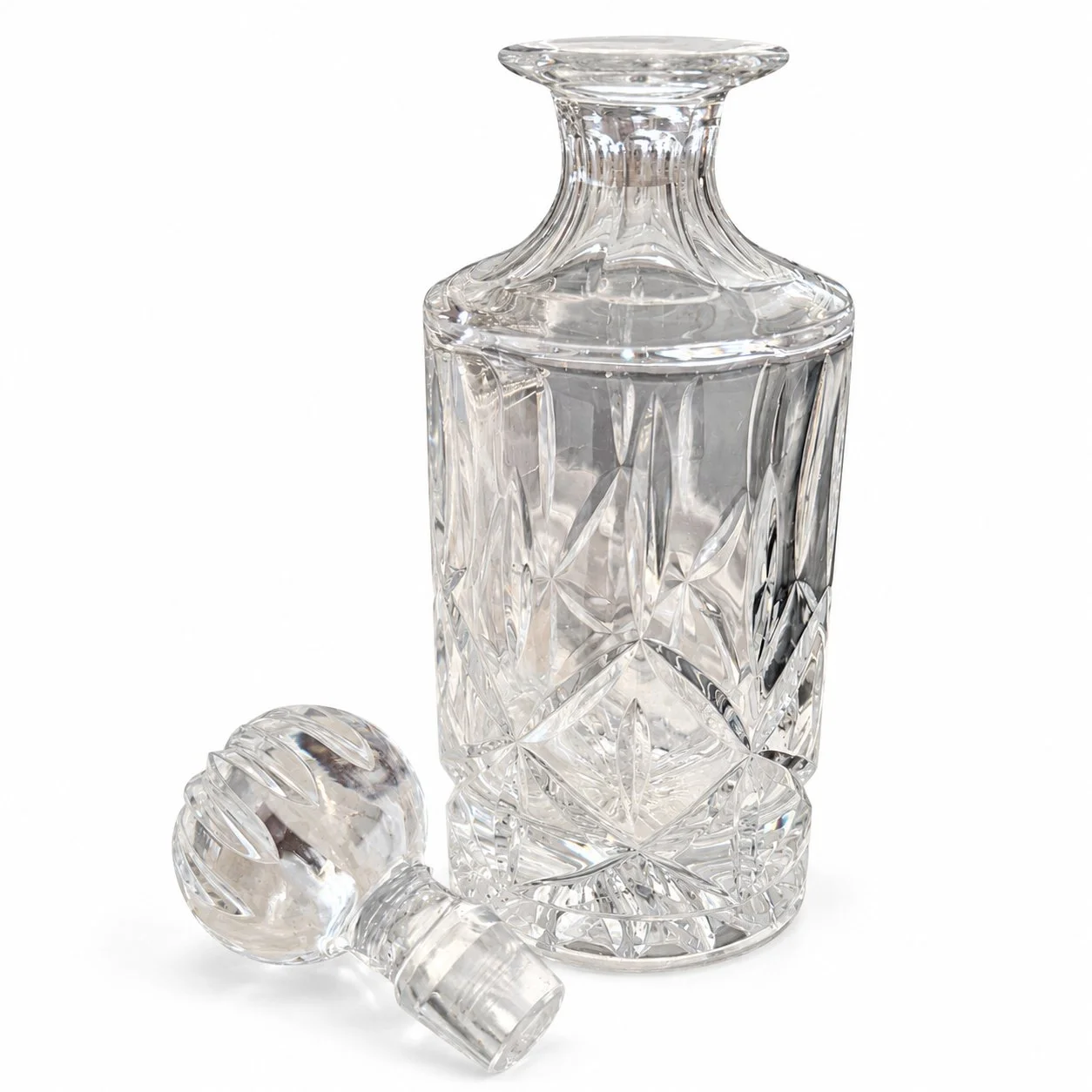 Clear decanter with its removable stopper placed beside it on white.