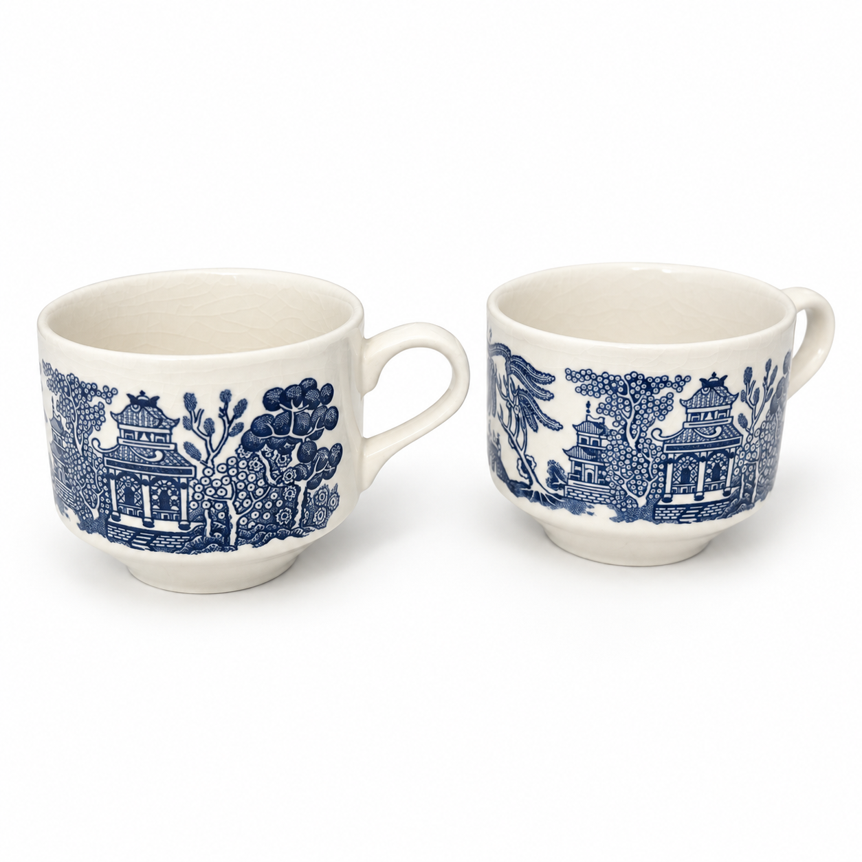 Two Blue Willow footed cups with navy pagoda scenes and cream handles on a white background.