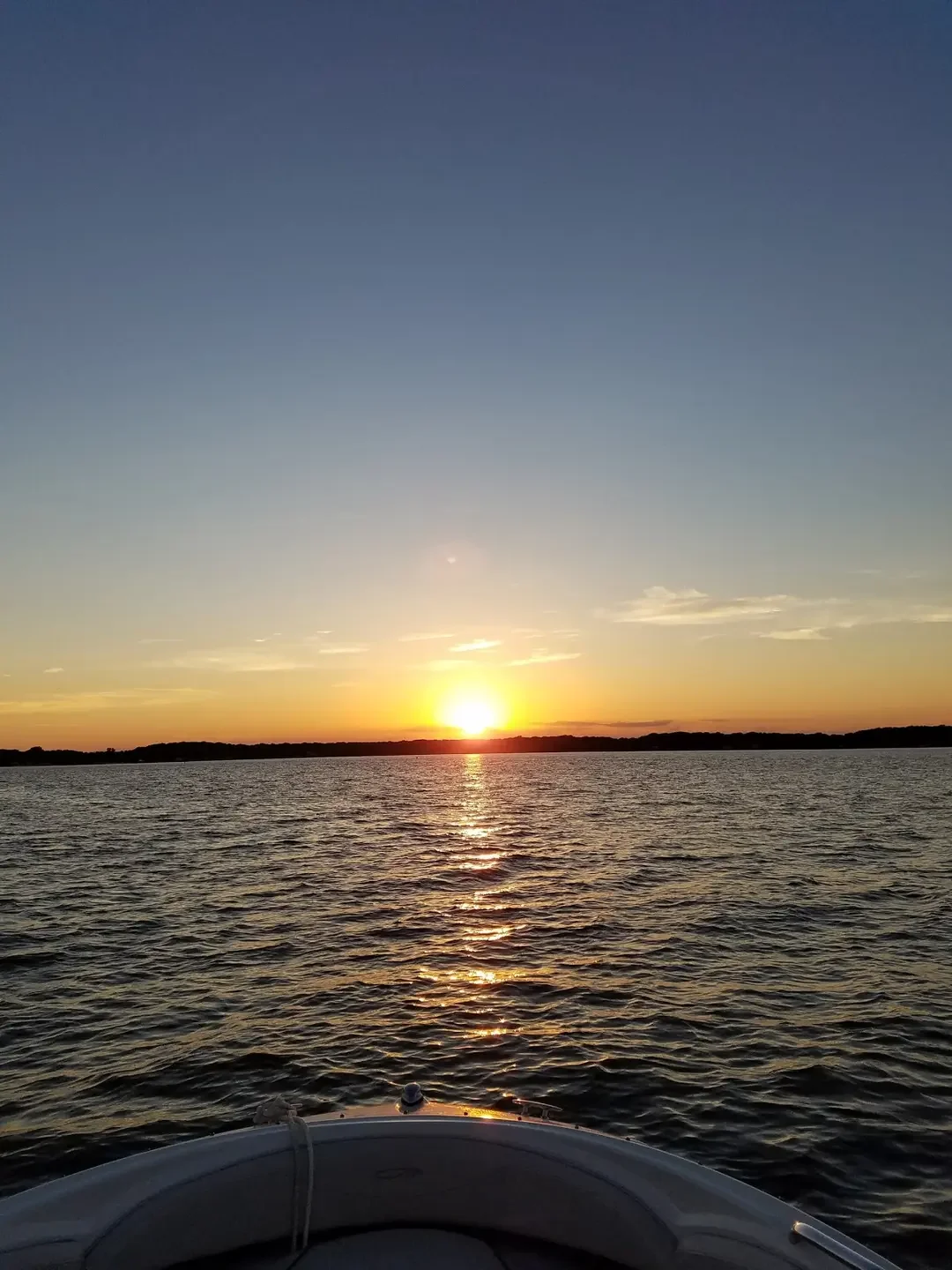 Sunset over a body of water, as viewed from a boat's bow.